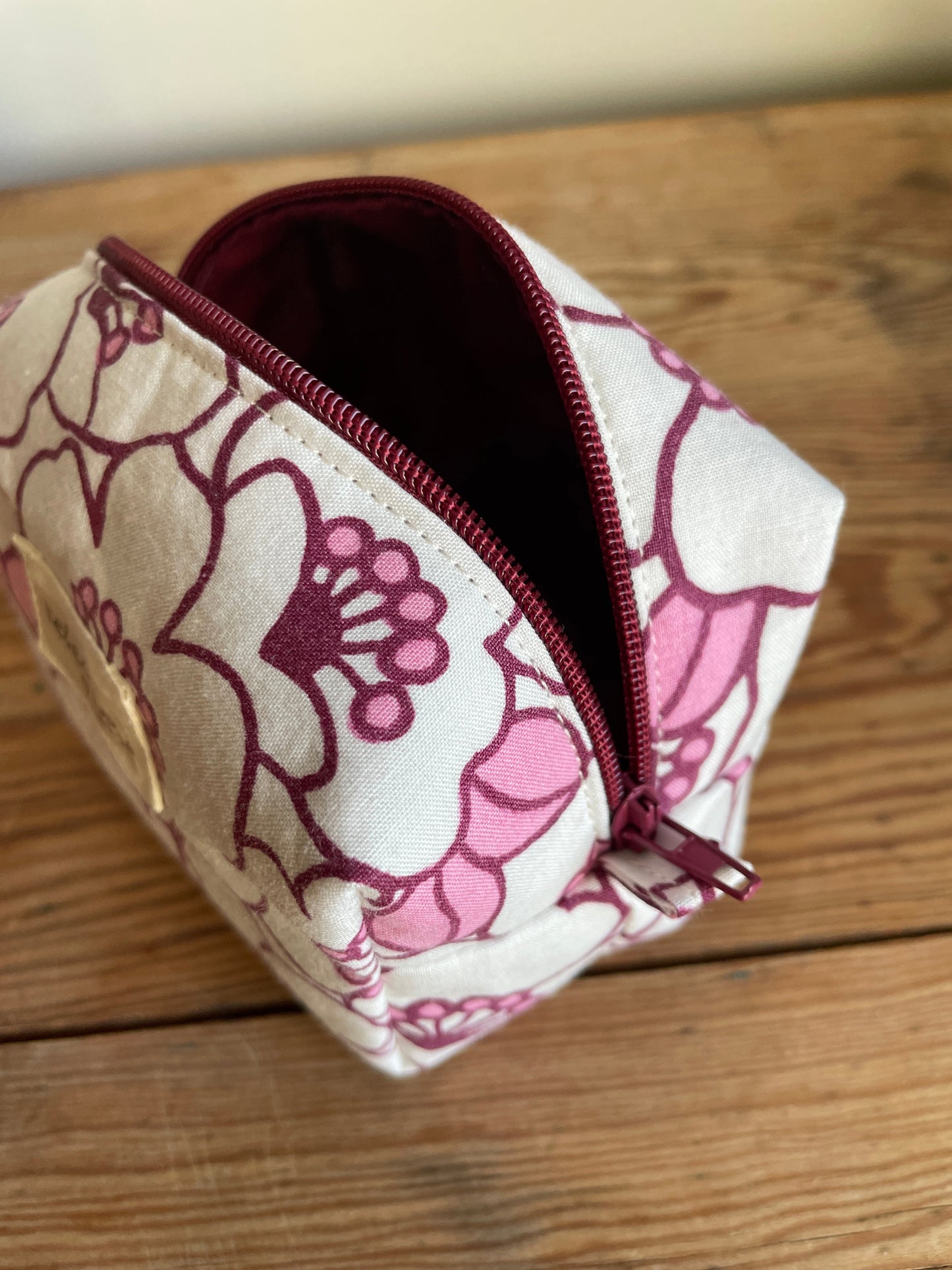 Blommig liten boxnecessär med stora vita och rosa blommor, vinröd dragkedja och vinrödrosa innerfoder.