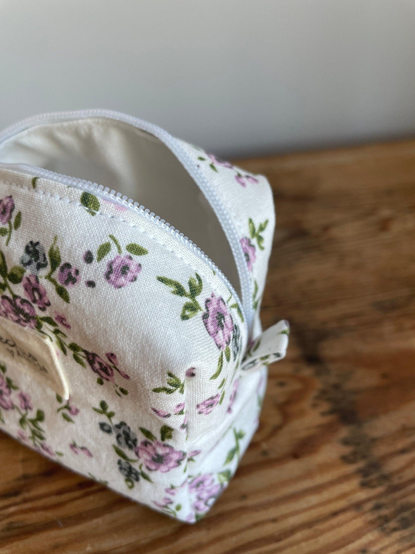 Handgjord mini boxnecessär i tyg med vit bakgrund, små lila blommor och vit dragkedja.