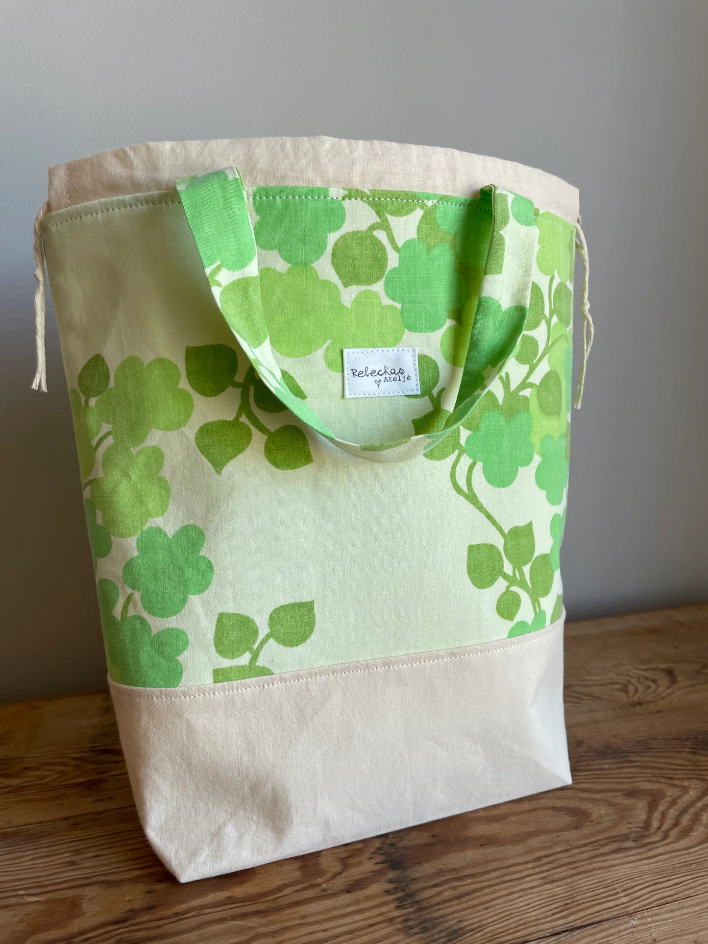 Projektväska mellan i ljusgult och grönt bomullstyg med retroinspirerat klövermönster i flera gröna nyanser. Handsydd projektpåse med dragskostängning och handtag, perfekt för stickning, virkning, garn och andra handarbetsprojekt. Den ljusgula bottenfärgen framhäver det gröna mönstret och ger väskan en ljus och somrig känsla.