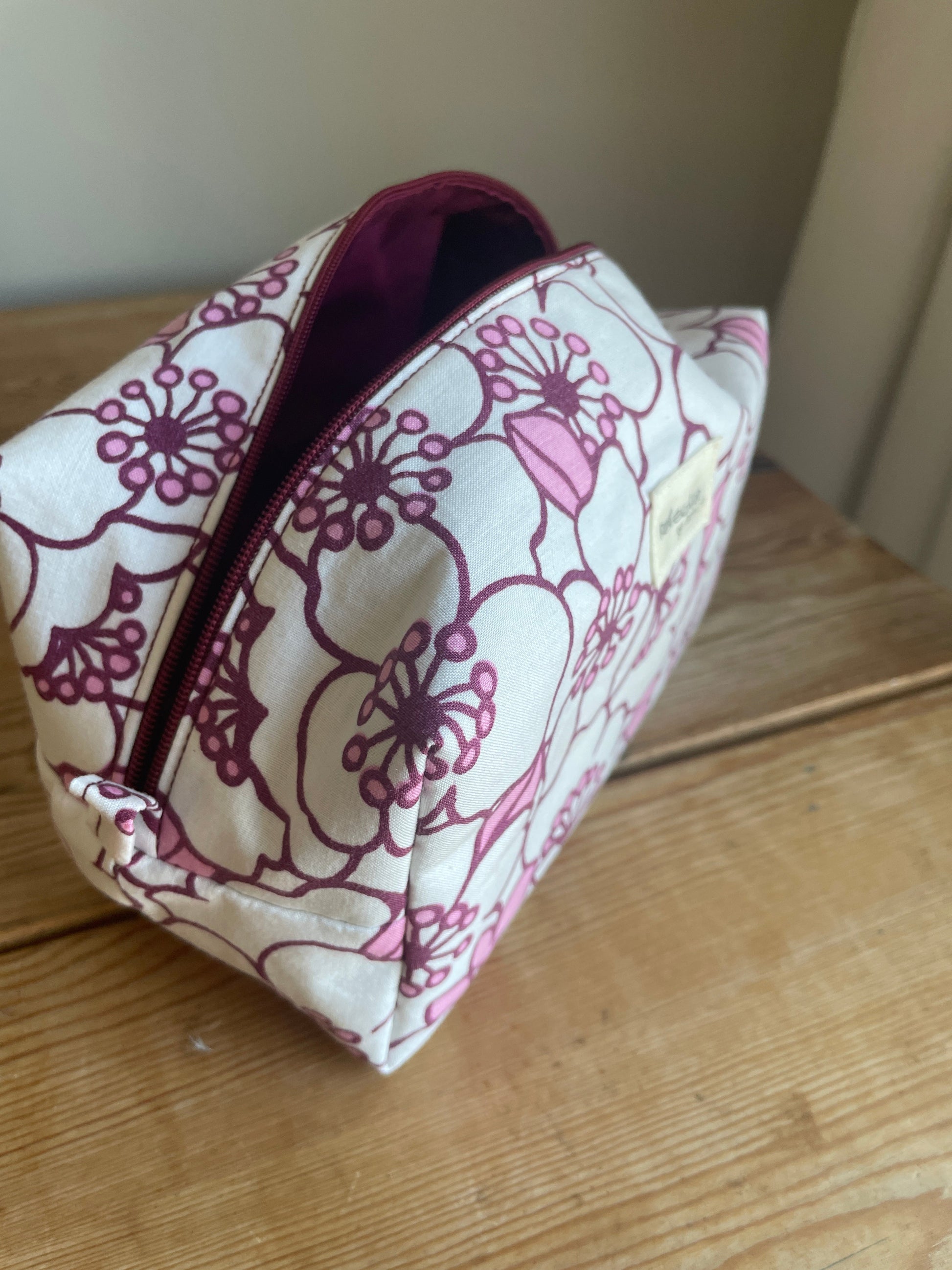 Blommig boxnecessär med stora vita och rosa blommor, vinröd dragkedja och vinrödrosa innerfoder.