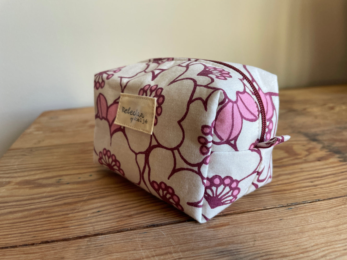 Blommig liten boxnecessär med stora vita och rosa blommor, vinröd dragkedja och vinrödrosa innerfoder.