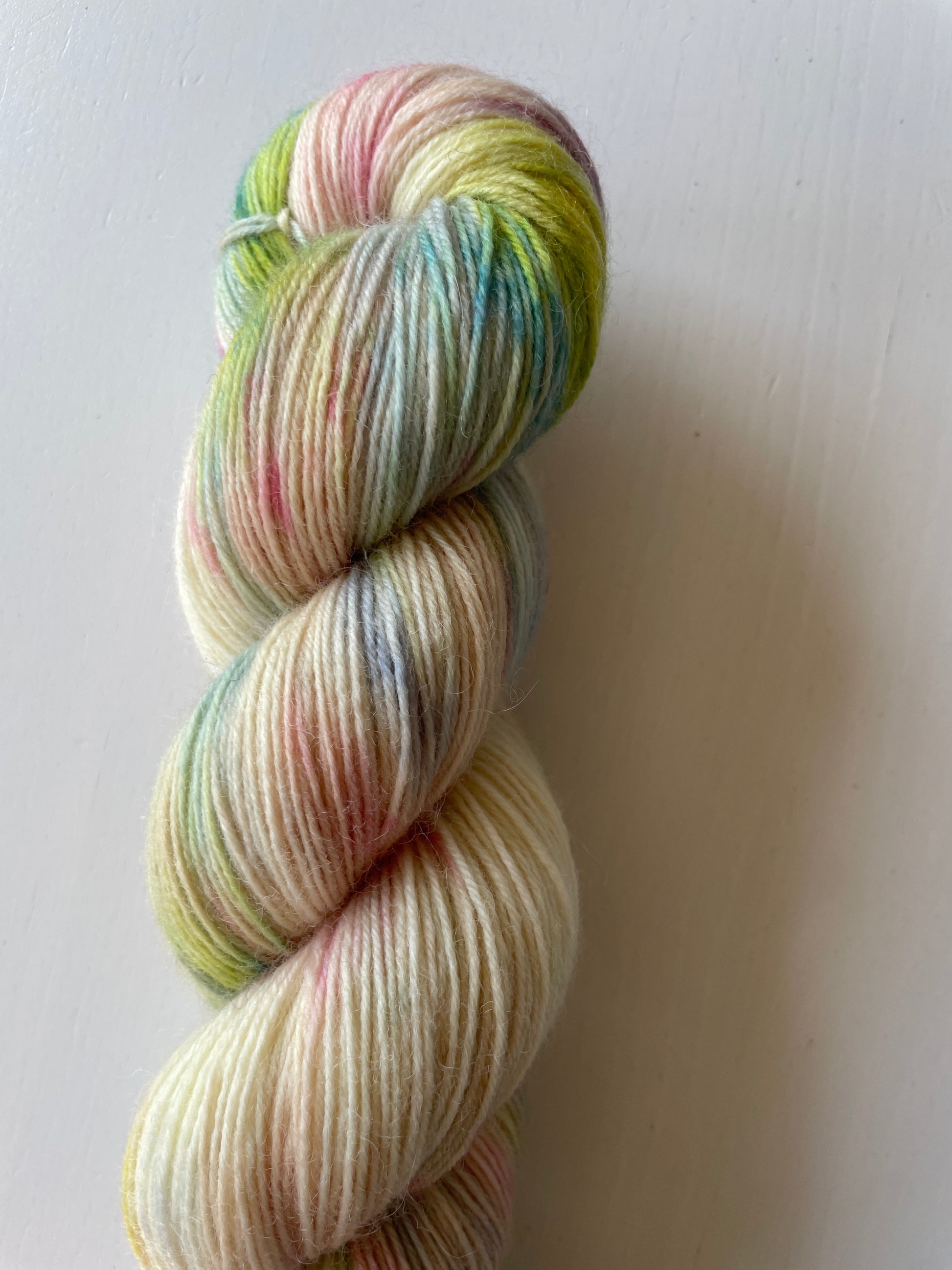 Handfärgat melerat garnnystan på 100 g i vitt och beige med färgstänk i gul, blå, rosa och grön samt ett blått miniskein på 20 g.