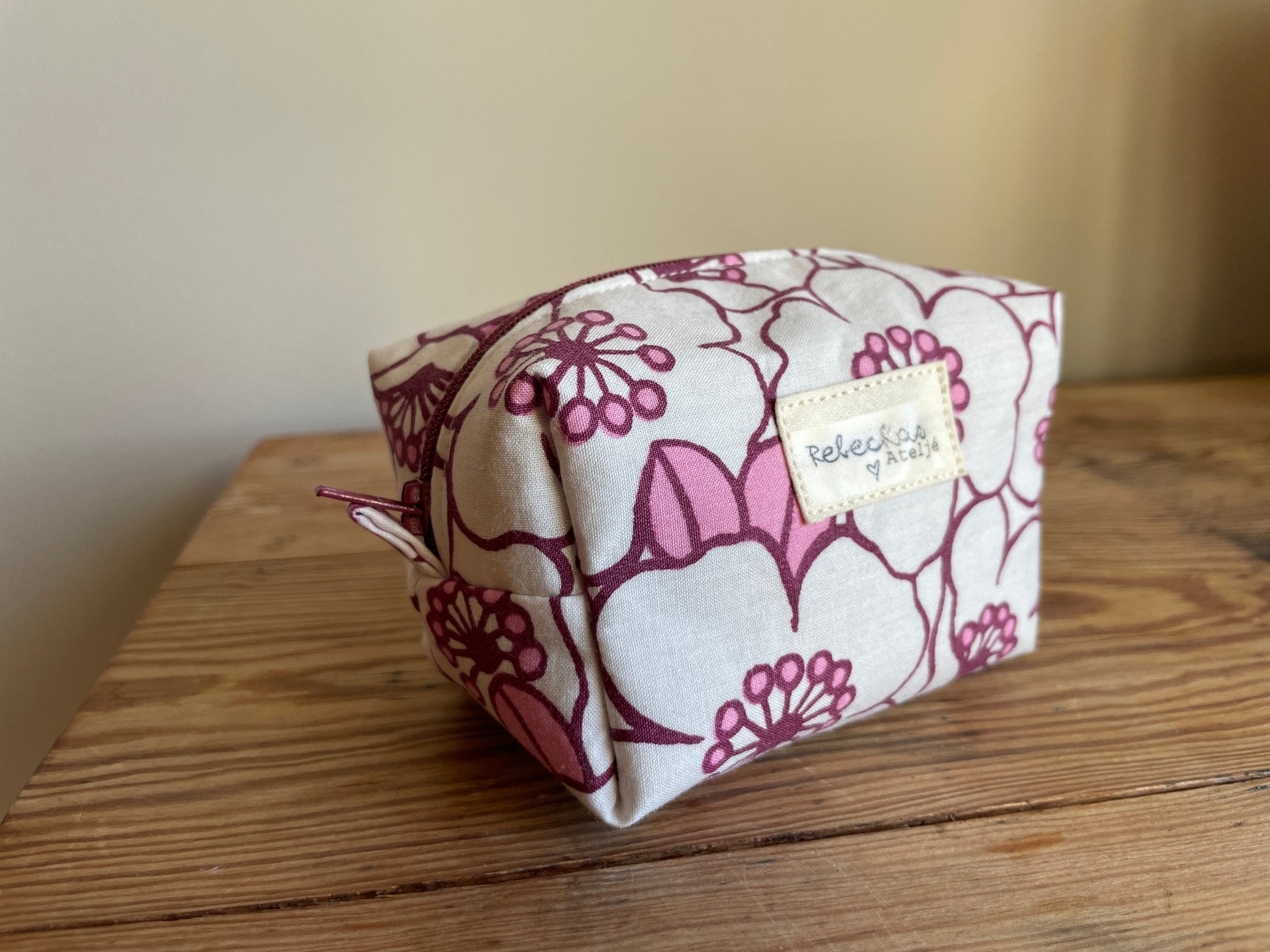 Blommig liten boxnecessär med stora vita och rosa blommor, vinröd dragkedja och vinrödrosa innerfoder.