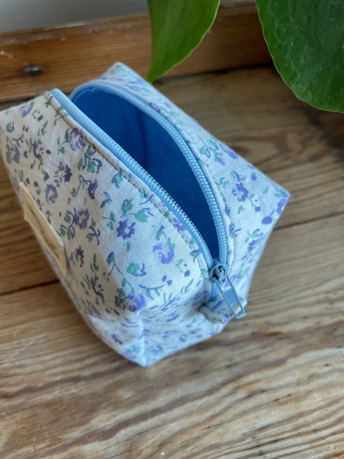 Mini boxnecessär i vitt tyg med ljusblå blommor, ljusblå dragkedja och ljusblått foder.
