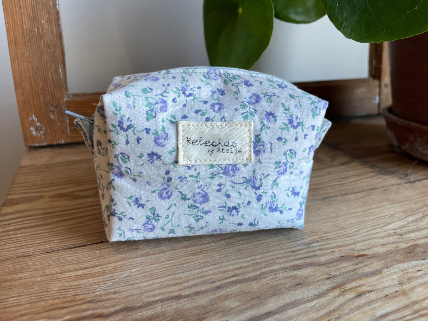 Mini boxnecessär i vitt tyg med ljusblå blommor, ljusblå dragkedja och ljusblått foder.