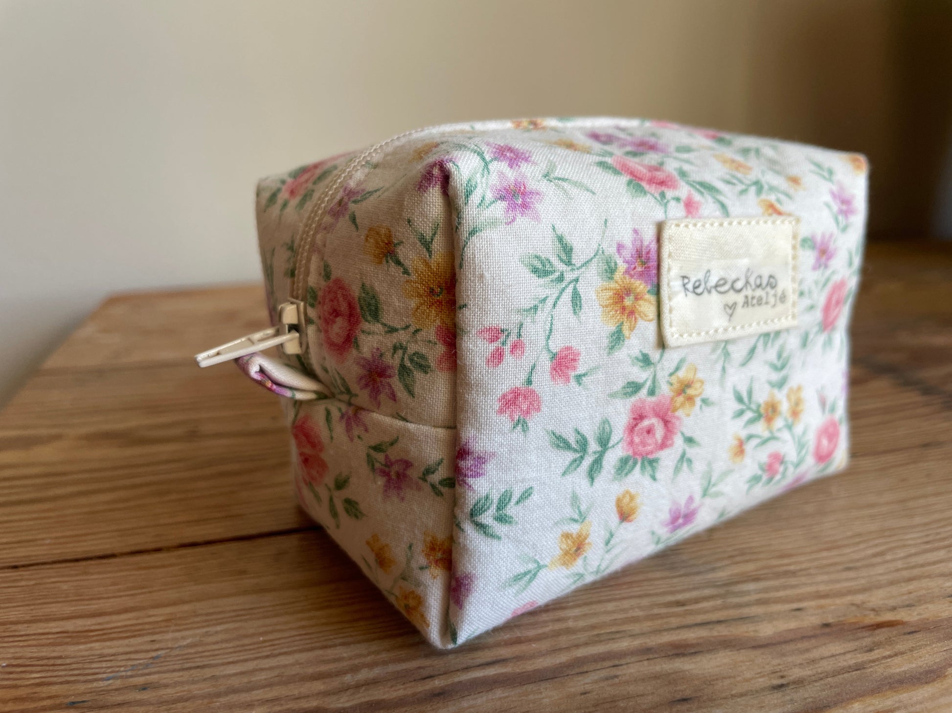Mini boxnecessär i vitt blommigt tyg med ljusa färgglada blommor och vit dragkedja.