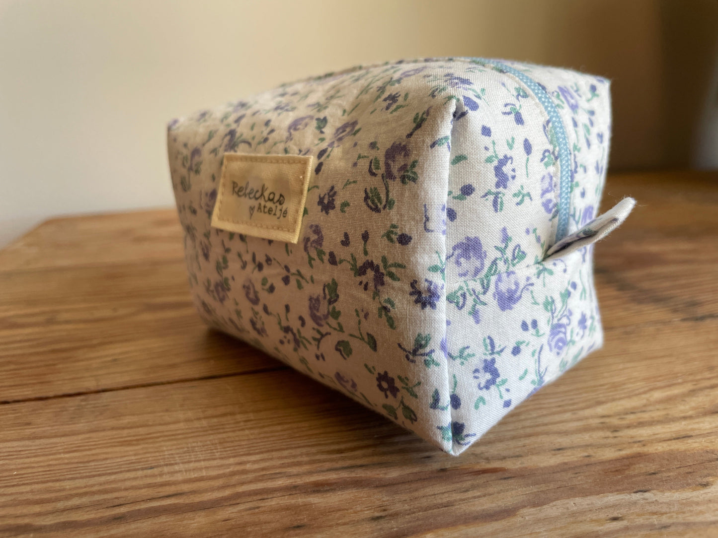 Mini boxnecessär i vitt tyg med ljusblå blommor, ljusblå dragkedja och ljusblått foder.