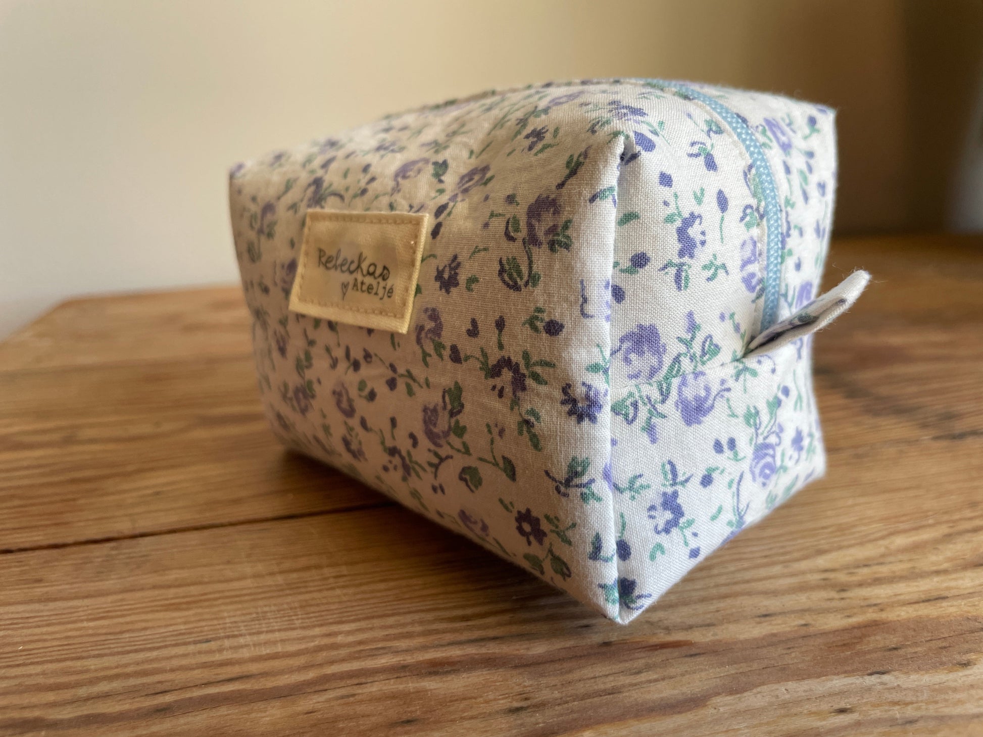Mini boxnecessär i vitt tyg med ljusblå blommor, ljusblå dragkedja och ljusblått foder.