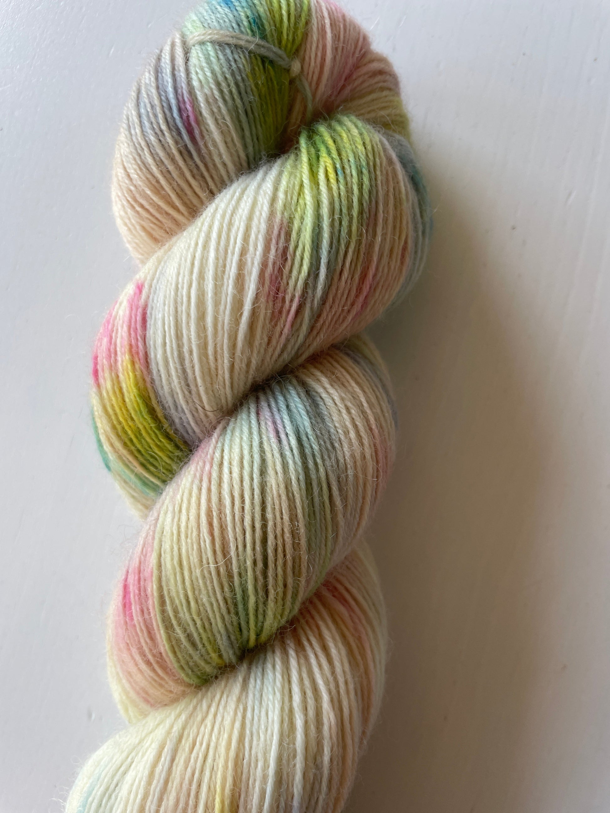 Handfärgat melerat garnnystan på 100 g i vitt och beige med färgstänk i gul, blå, rosa och grön samt ett blått miniskein på 20 g.