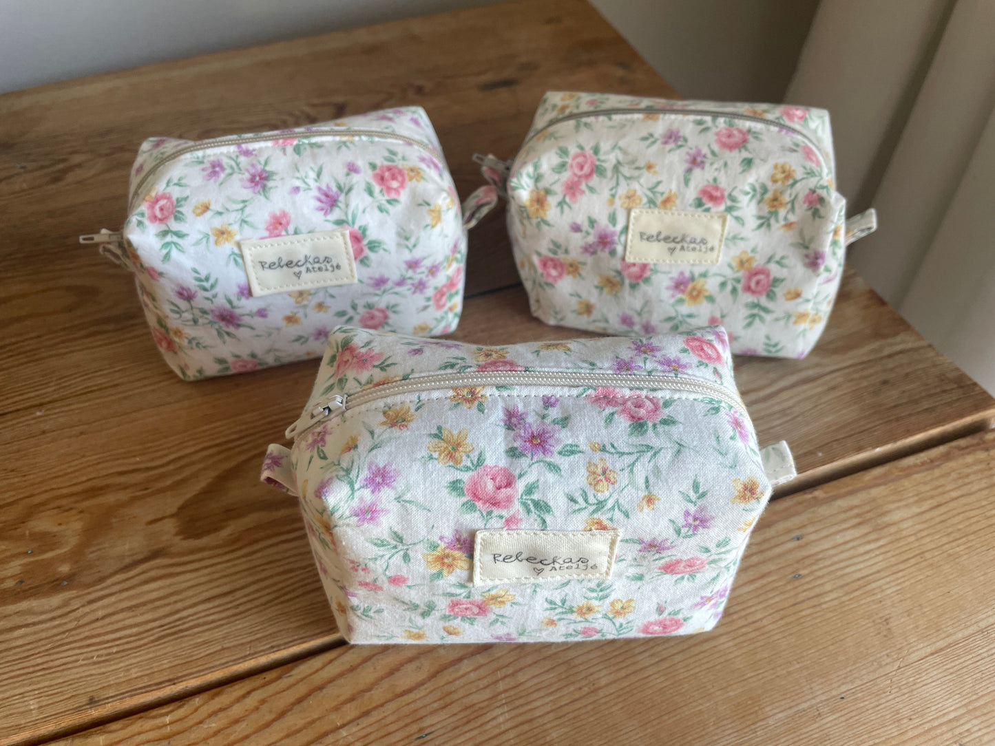 tre stycken Mini boxnecessär i vitt blommigt tyg med ljusa färgglada blommor och vit dragkedja.