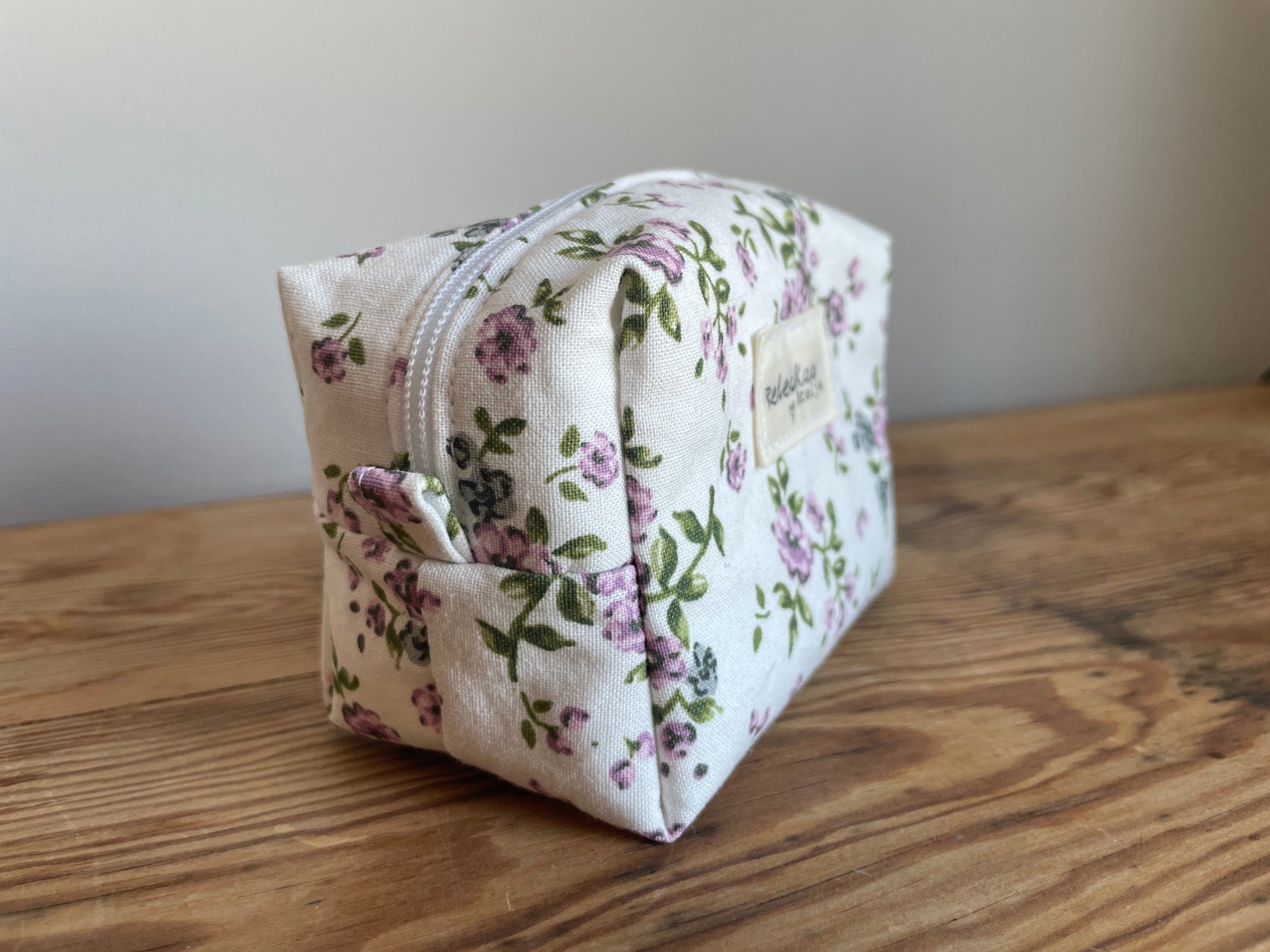 Handgjord mini boxnecessär i tyg med vit bakgrund, små lila blommor och vit dragkedja.