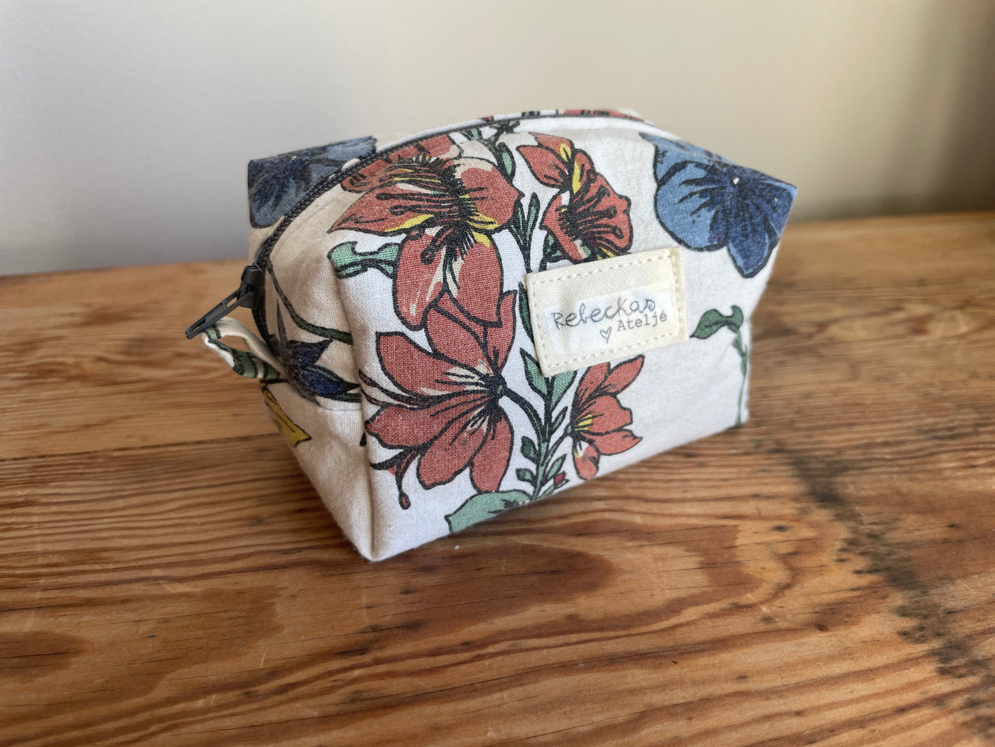 Handgjord mini boxnecessär i storblommigt tyg med vit bakgrund och flerfärgade blommor. mörkgrå dragkedja