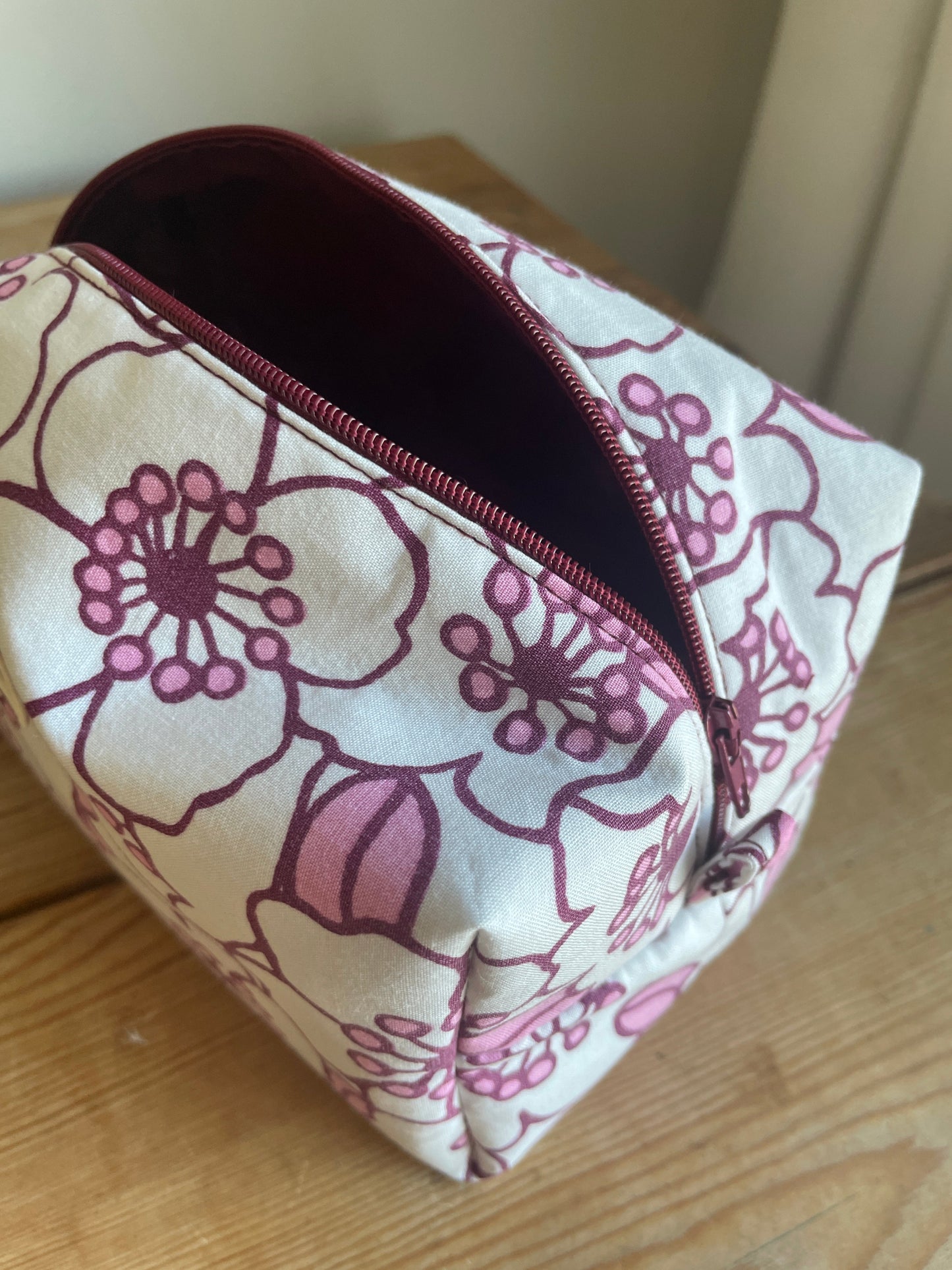 Blommig boxnecessär med stora vita och rosa blommor, vinröd dragkedja och vinrödrosa innerfoder.