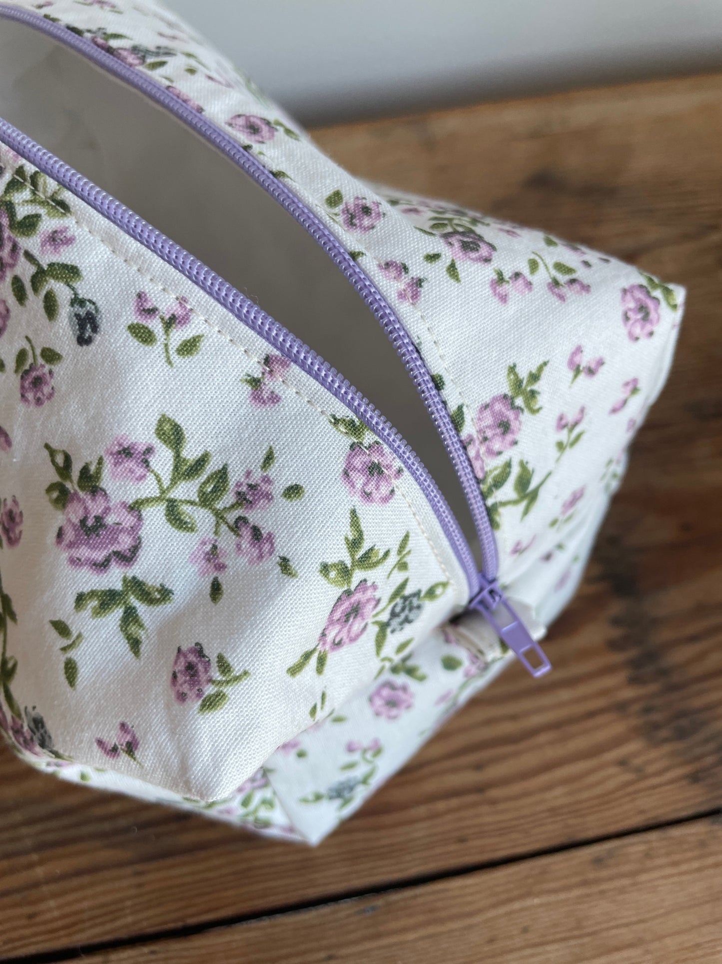 Handgjord boxnecessär i tyg med vit bakgrund, små lila blommor och lila dragkedja.