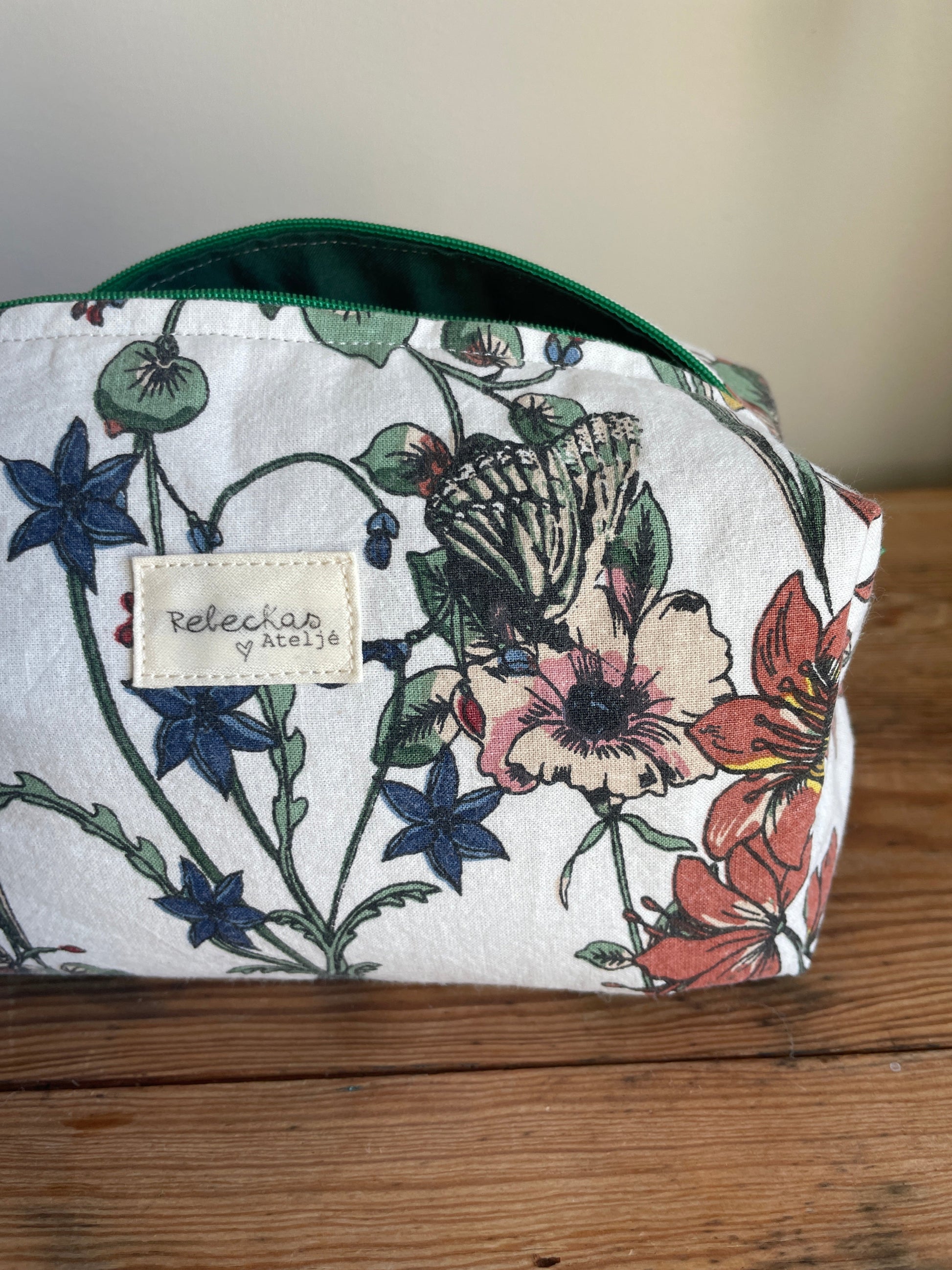 Handgjord boxnecessär i storblommigt tyg med vit bakgrund och flerfärgade blommor. mörkgrön dragkedja