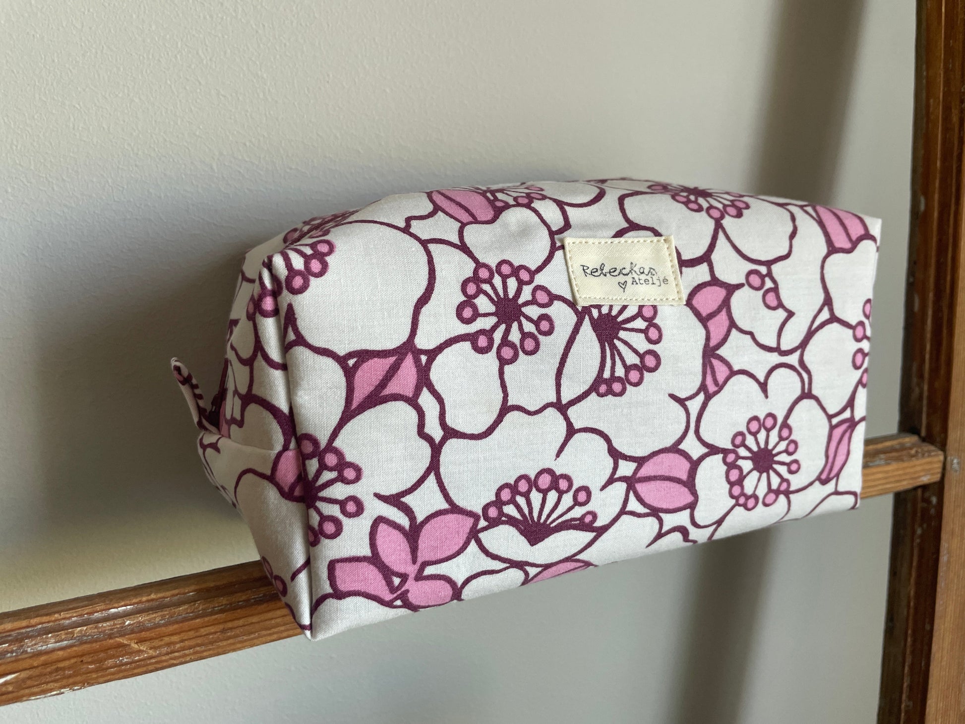 Blommig boxnecessär med stora vita och rosa blommor, vinröd dragkedja och vinrödrosa innerfoder.