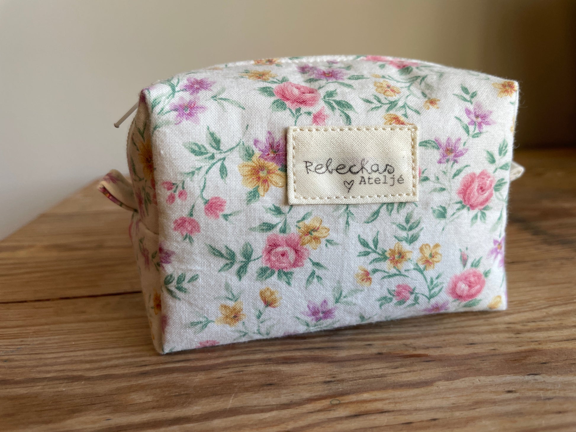 Mini boxnecessär i vitt blommigt tyg med ljusa färgglada blommor och vit dragkedja.