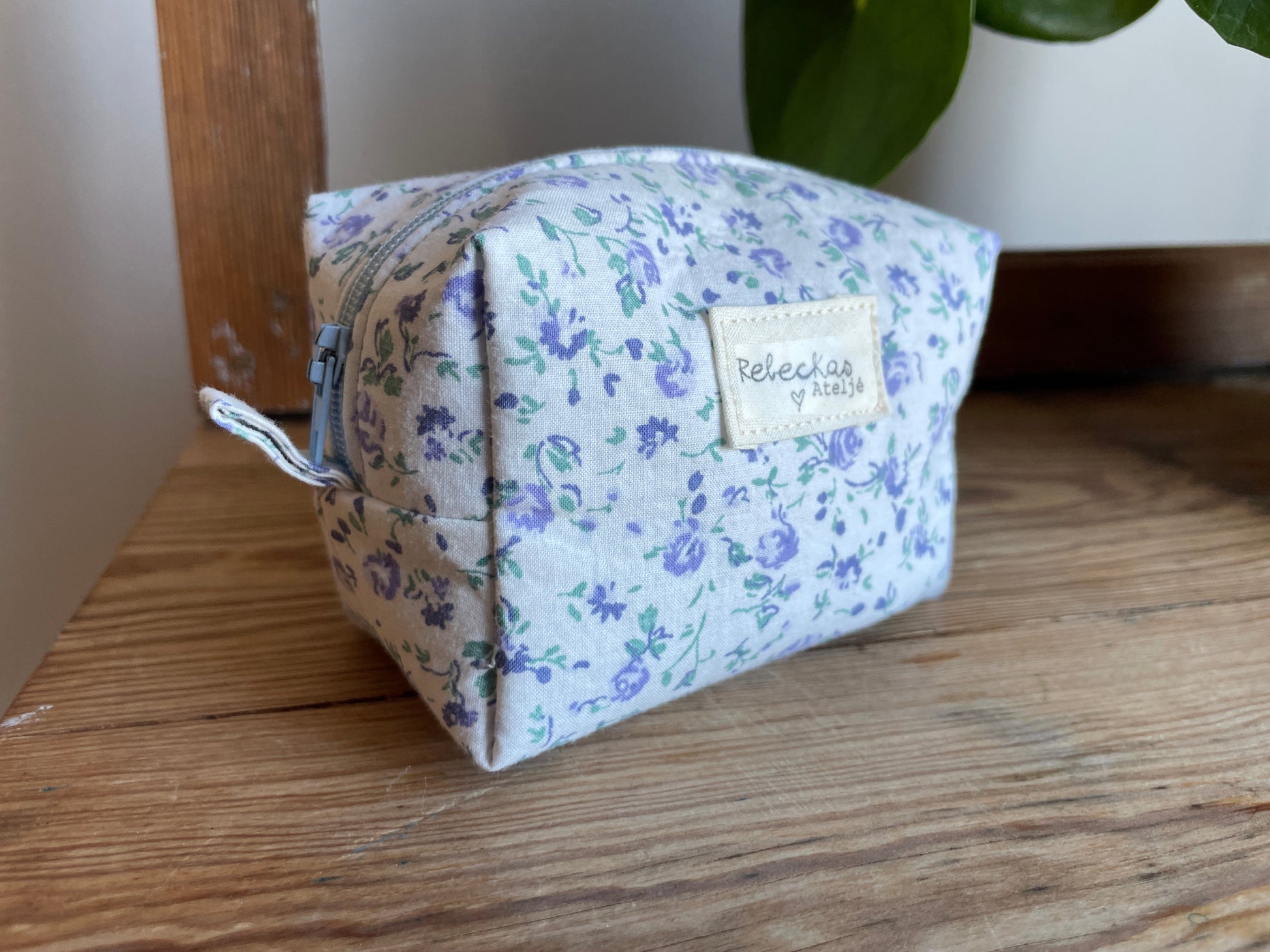 Mini boxnecessär i vitt tyg med ljusblå blommor, ljusblå dragkedja och ljusblått foder.