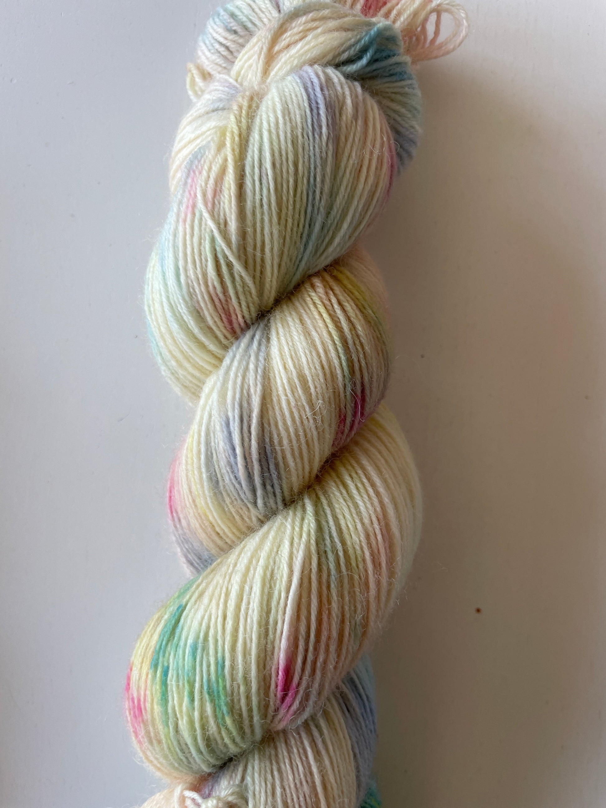 Handfärgat melerat garnnystan på 100 g i vitt och beige med färgstänk i gul, blå, rosa och grön samt ett blått miniskein på 20 g.