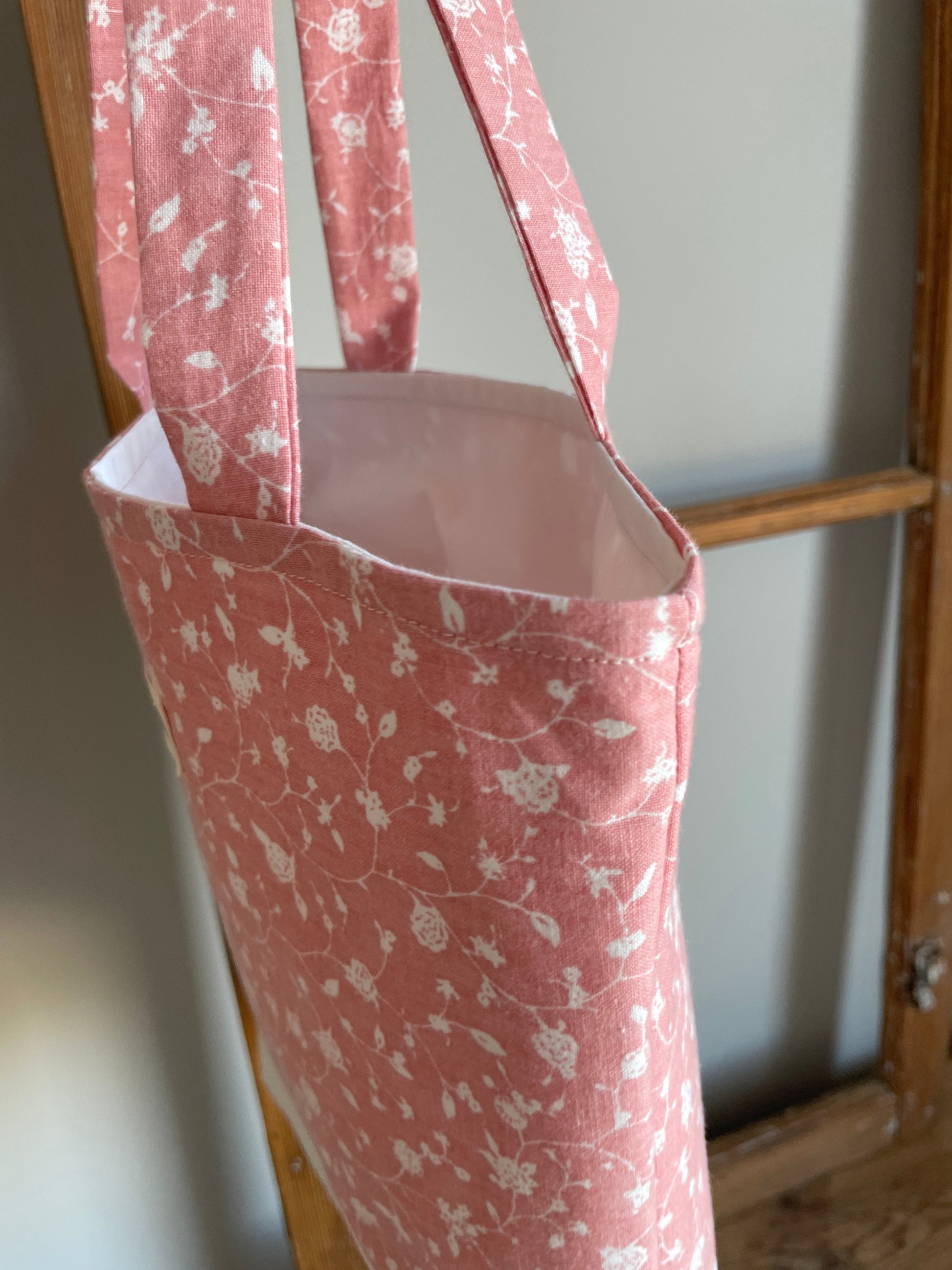 tygväska med vit botten och rosa blommönster hängande på gammal fönsterram. vitt foder