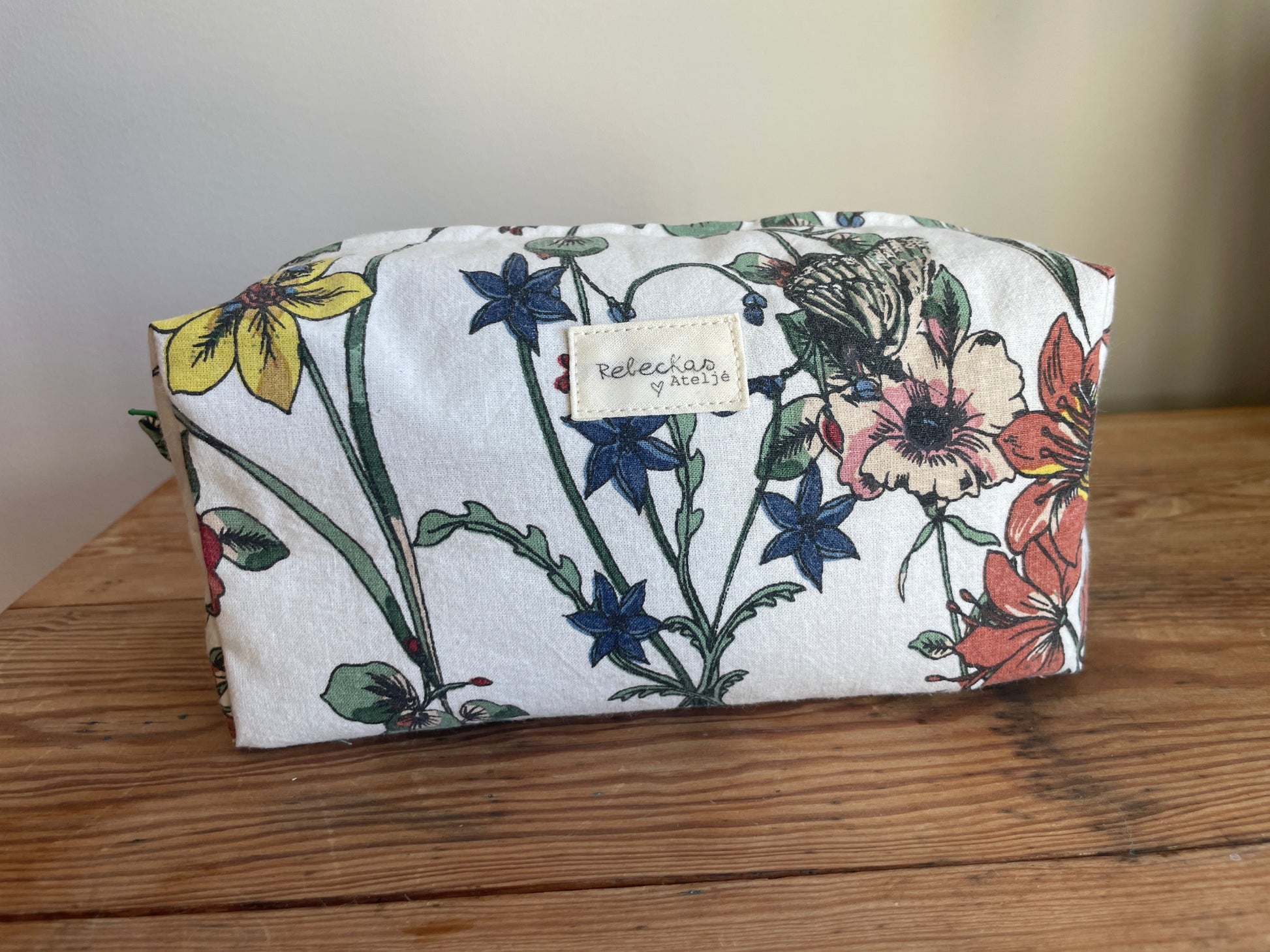 Handgjord boxnecessär i storblommigt tyg med vit bakgrund och flerfärgade blommor. mörkgrön dragkedja