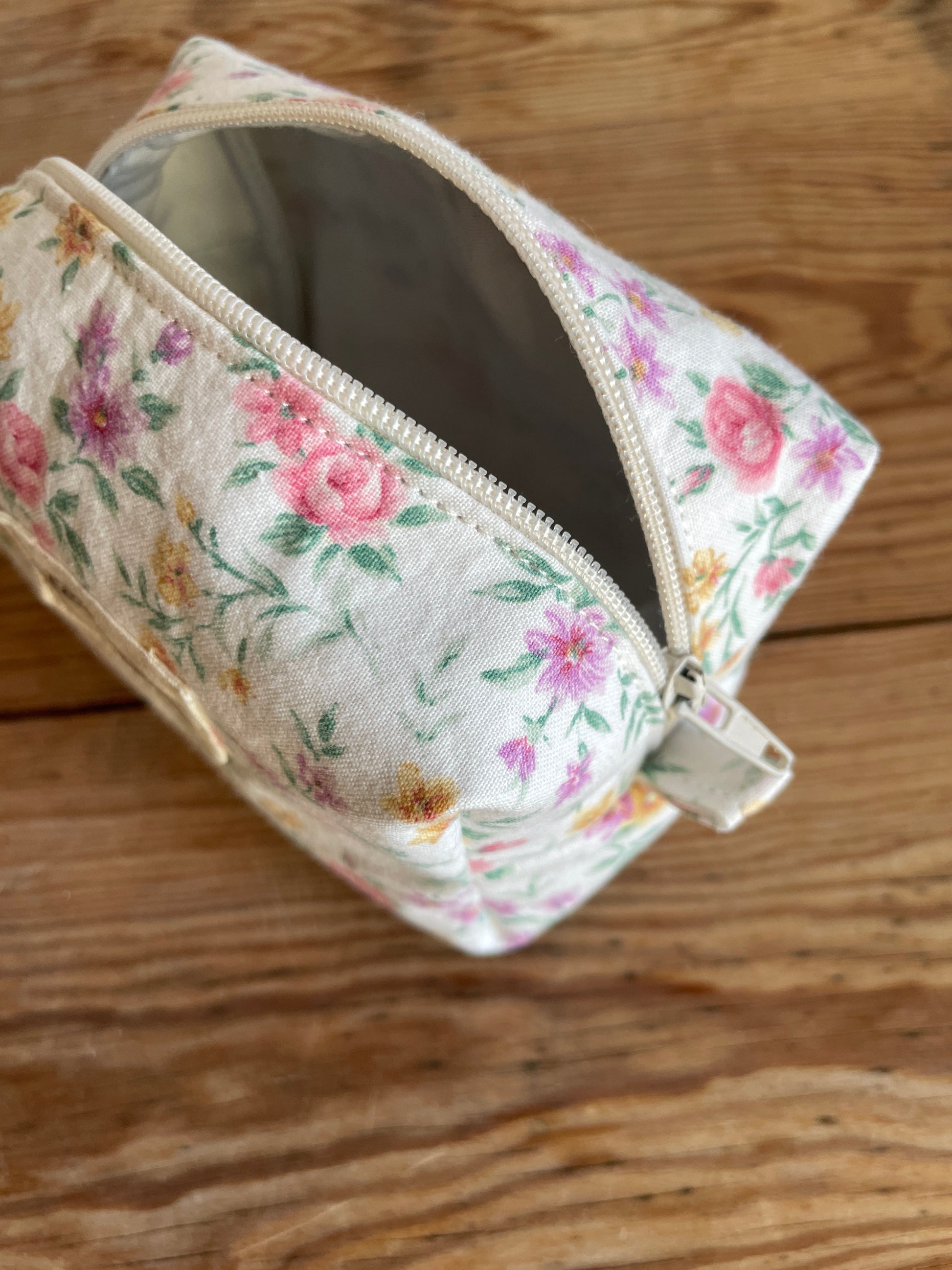 Mini boxnecessär i vitt blommigt tyg med ljusa färgglada blommor och vit dragkedja.