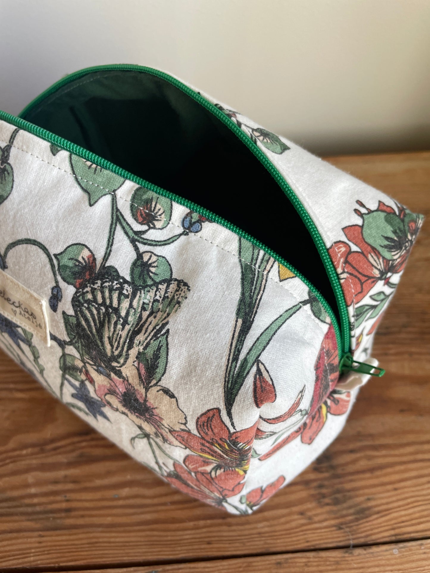 Handgjord boxnecessär i storblommigt tyg med vit bakgrund och flerfärgade blommor. mörkgrön dragkedja