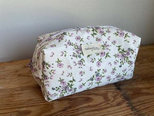 Handgjord boxnecessär i tyg med vit bakgrund, små lila blommor och lila dragkedja.