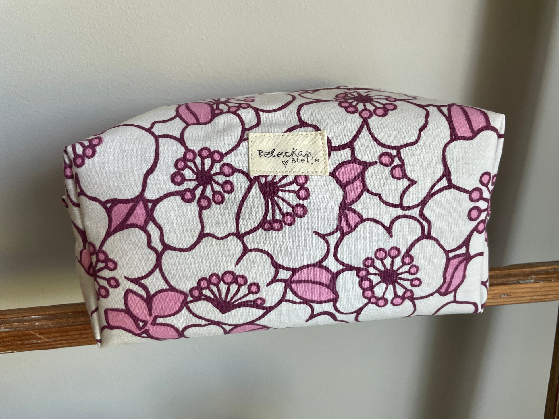 Blommig boxnecessär med stora vita och rosa blommor, vinröd dragkedja och vinrödrosa innerfoder.