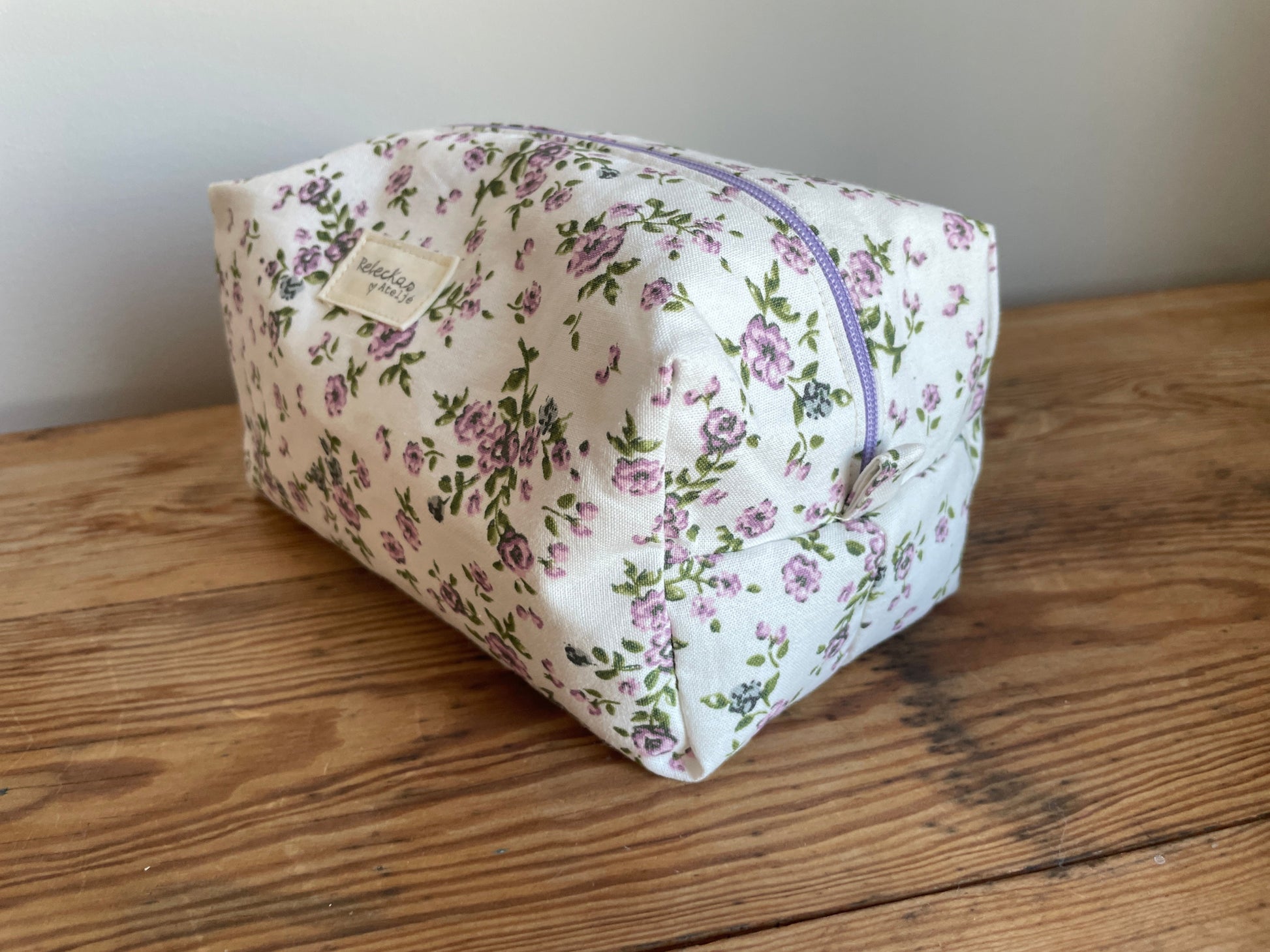 Handgjord boxnecessär i tyg med vit bakgrund, små lila blommor och lila dragkedja.