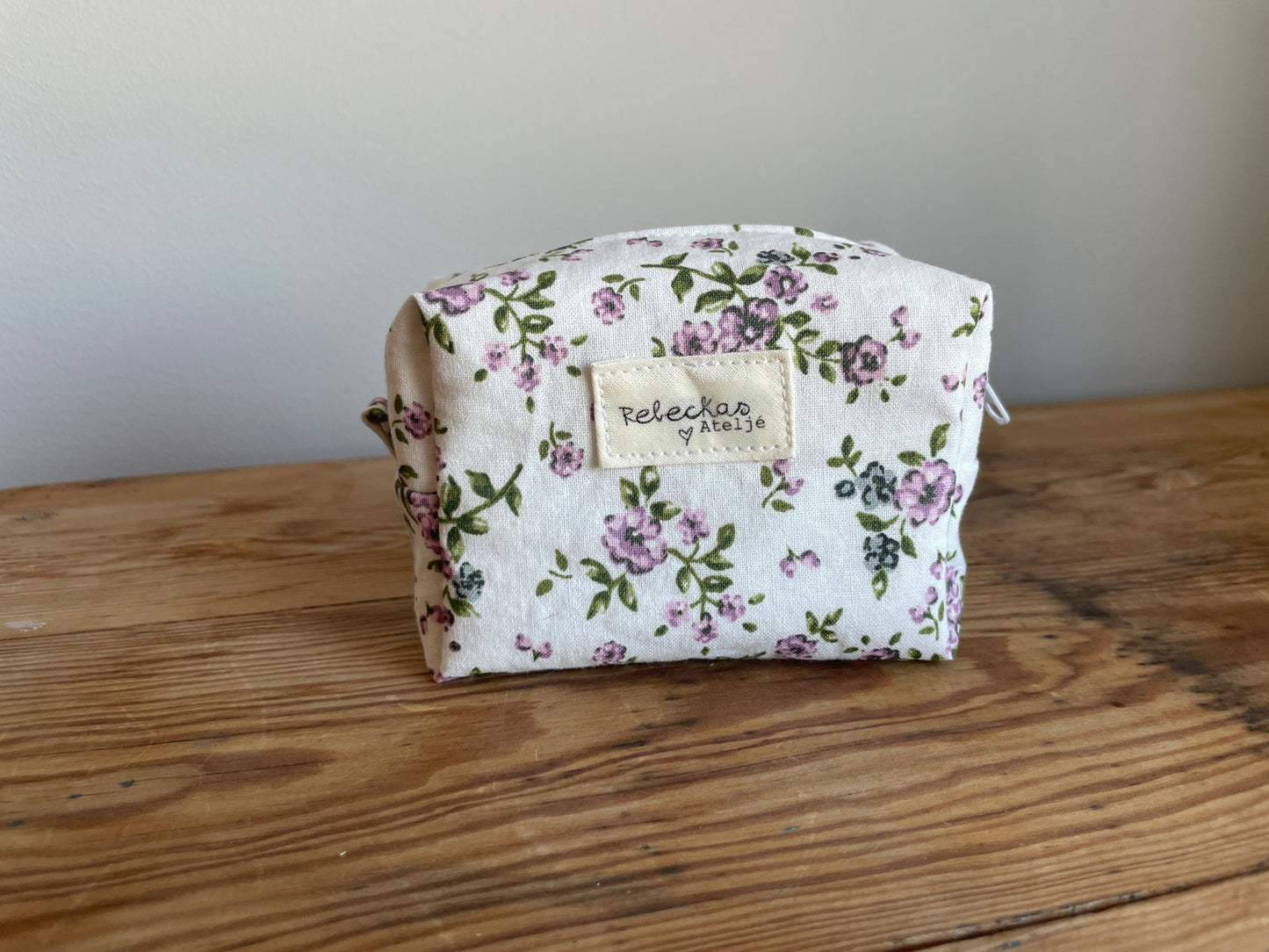 Handgjord mini boxnecessär i tyg med vit bakgrund, små lila blommor och vit dragkedja.