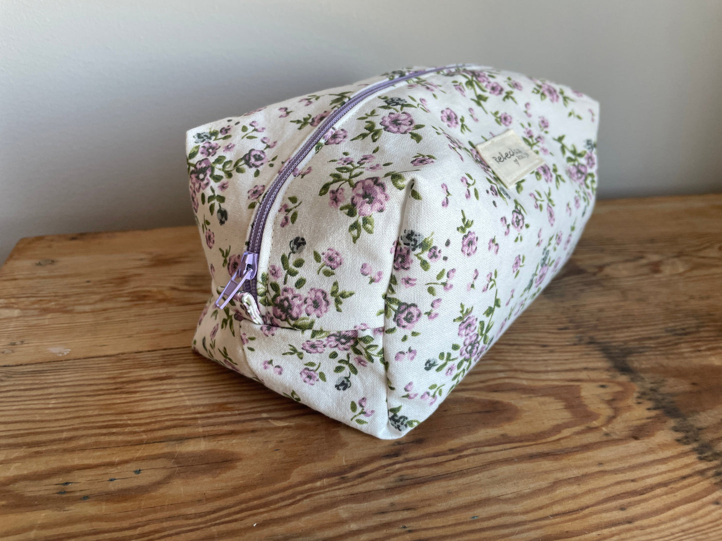 Handgjord boxnecessär i tyg med vit bakgrund, små lila blommor och lila dragkedja.