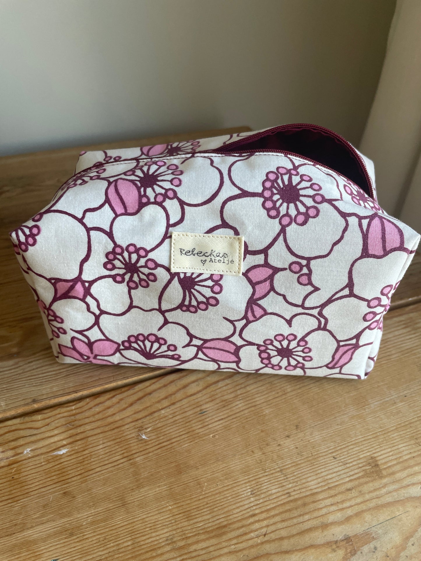 Blommig boxnecessär med stora vita och rosa blommor, vinröd dragkedja och vinrödrosa innerfoder.