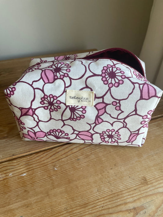 Blommig boxnecessär med stora vita och rosa blommor, vinröd dragkedja och vinrödrosa innerfoder.