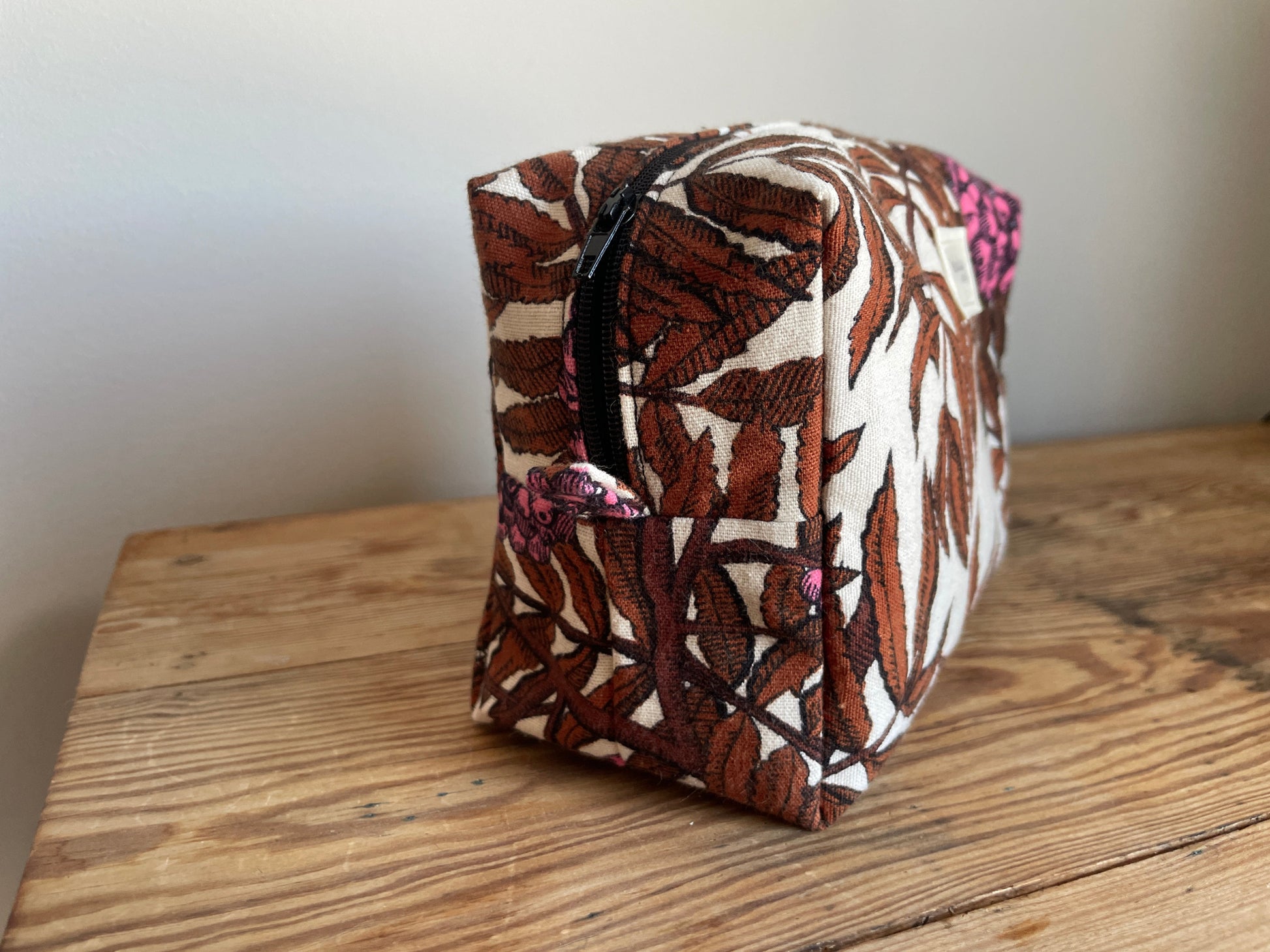 Handgjord boxnecessär i tyg med beige bakgrund, mörkbruna löv, starkt rosa bärklasar och dragkedja.