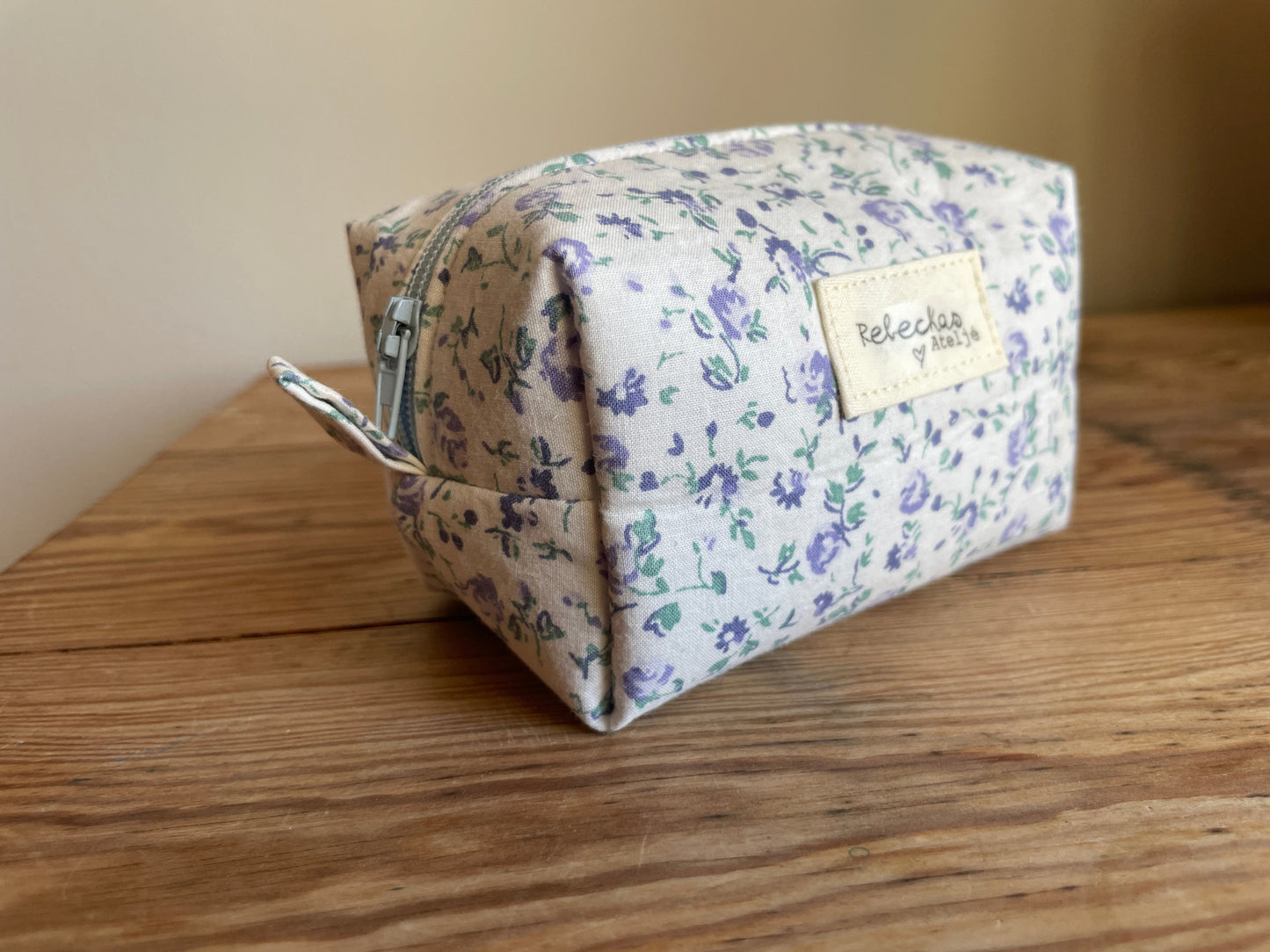 Mini boxnecessär i vitt tyg med ljusblå blommor, ljusblå dragkedja och ljusblått foder.