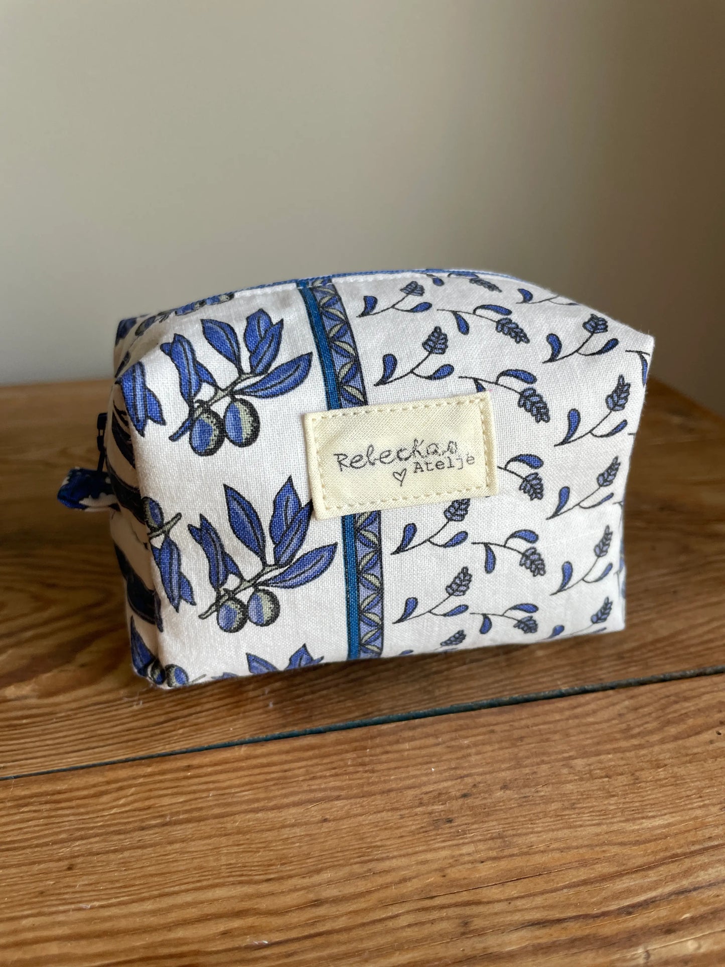 Mini boxnecessär i vitt tyg med blått blommönster och olivkvistar, handsydd med blå dragkedja.