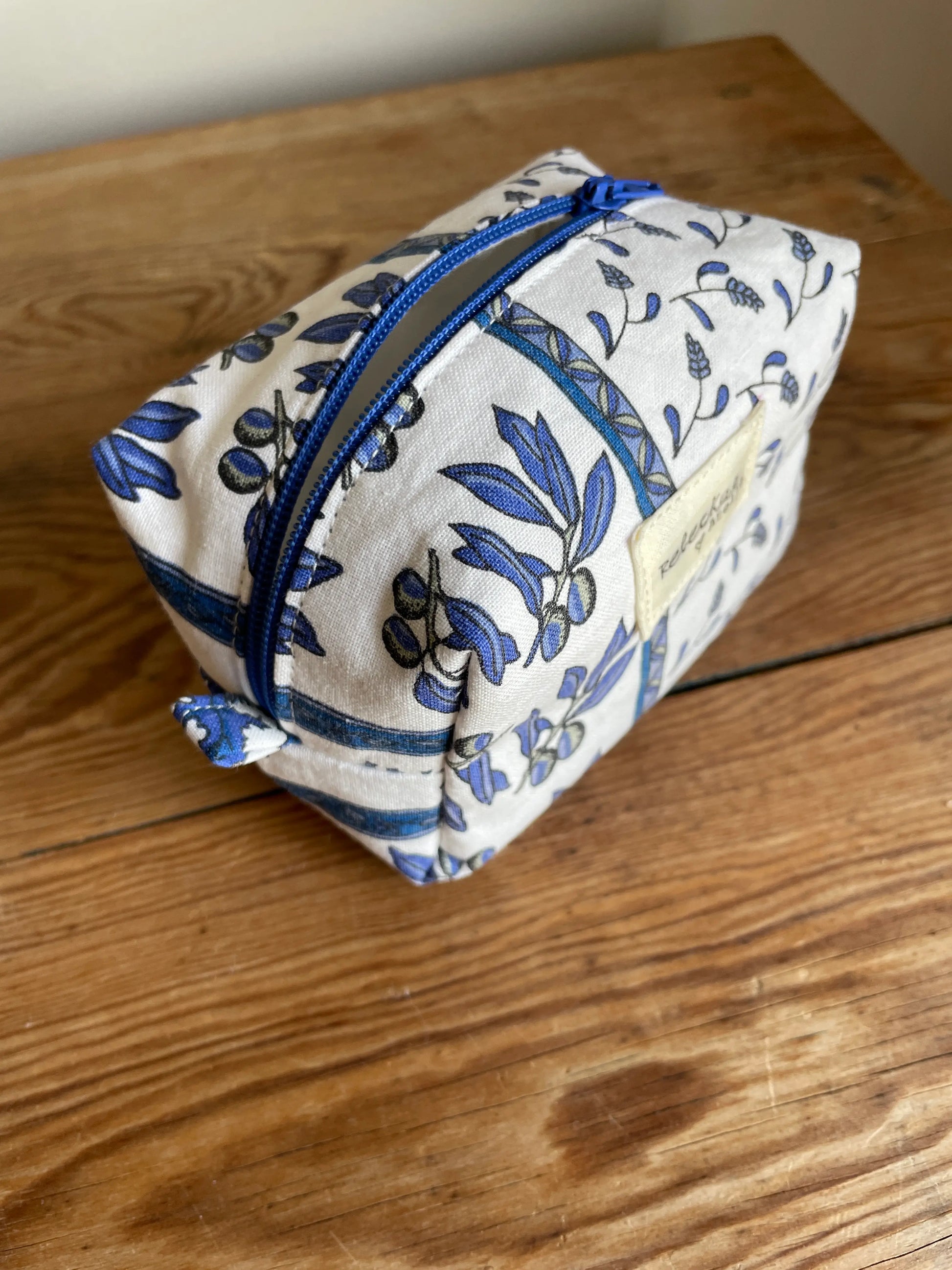 Mini boxnecessär i vitt tyg med blått blommönster och olivkvistar, handsydd med blå dragkedja.