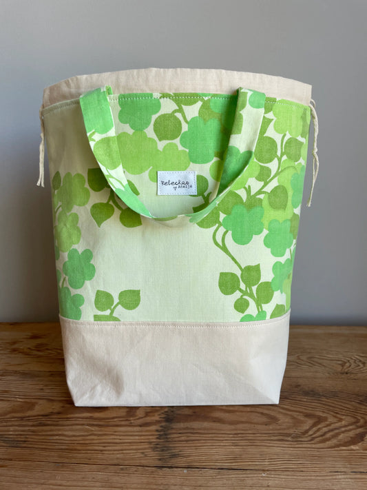 Projektväska mellan i ljusgult och grönt bomullstyg med retroinspirerat klövermönster i flera gröna nyanser. Handsydd projektpåse med dragskostängning och handtag, perfekt för stickning, virkning, garn och andra handarbetsprojekt. Den ljusgula bottenfärgen framhäver det gröna mönstret och ger väskan en ljus och somrig känsla.