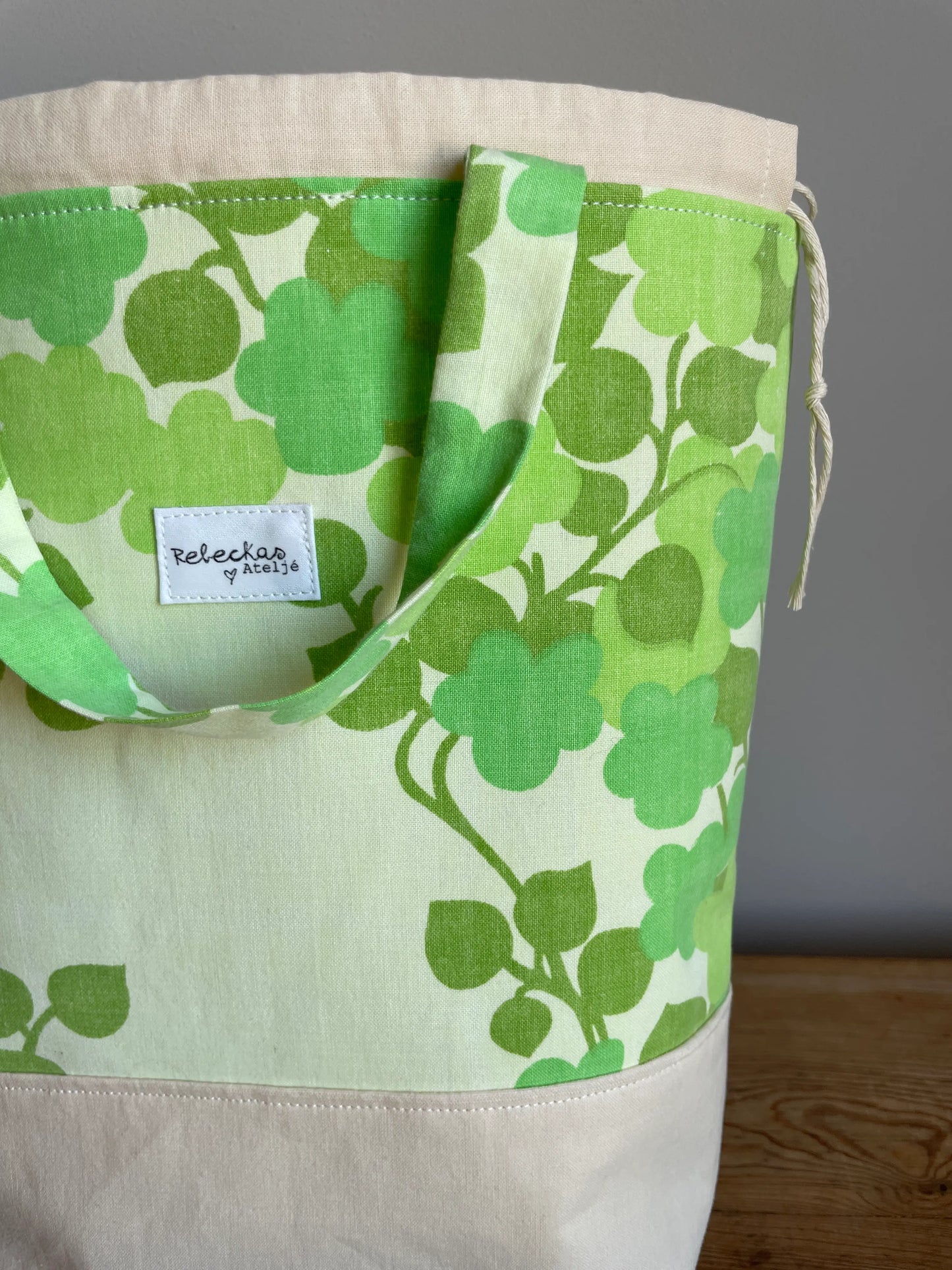 Projektväska mellan i ljusgult och grönt bomullstyg med retroinspirerat klövermönster i flera gröna nyanser. Handsydd projektpåse med dragskostängning och handtag, perfekt för stickning, virkning, garn och andra handarbetsprojekt. Den ljusgula bottenfärgen framhäver det gröna mönstret och ger väskan en ljus och somrig känsla.