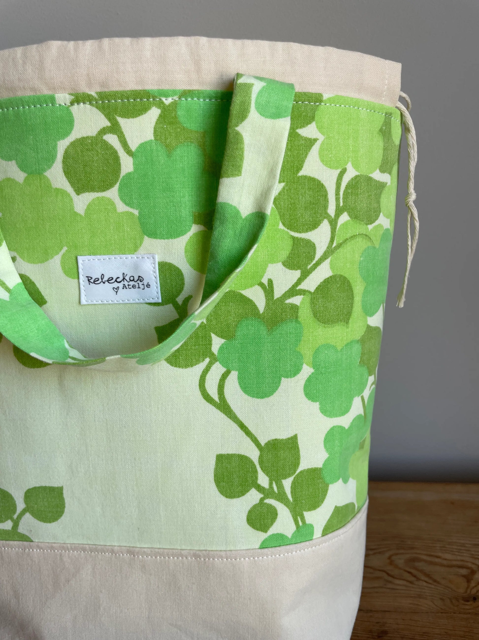 Projektväska mellan i ljusgult och grönt bomullstyg med retroinspirerat klövermönster i flera gröna nyanser. Handsydd projektpåse med dragskostängning och handtag, perfekt för stickning, virkning, garn och andra handarbetsprojekt. Den ljusgula bottenfärgen framhäver det gröna mönstret och ger väskan en ljus och somrig känsla.