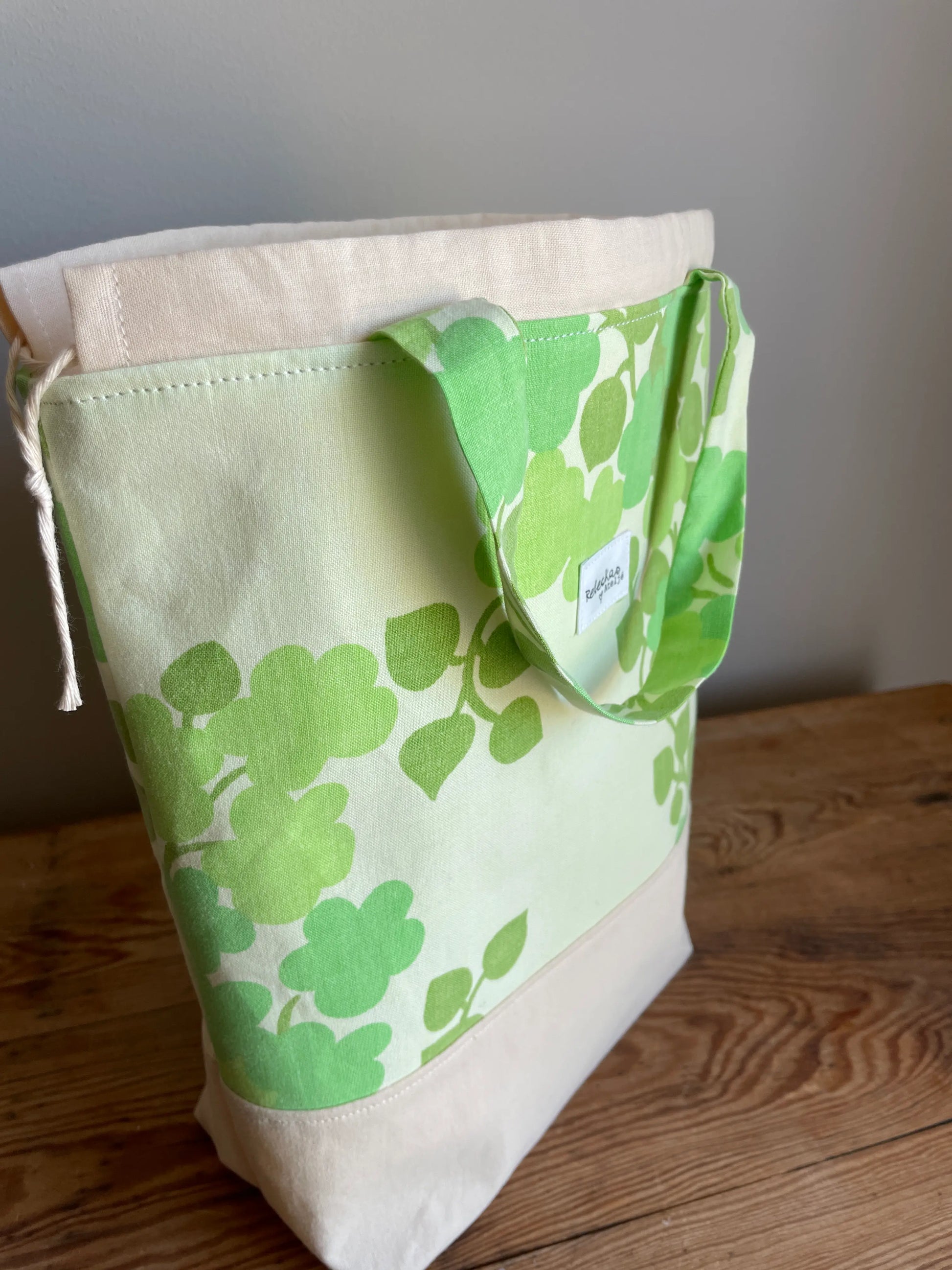 Projektväska mellan i ljusgult och grönt bomullstyg med retroinspirerat klövermönster i flera gröna nyanser. Handsydd projektpåse med dragskostängning och handtag, perfekt för stickning, virkning, garn och andra handarbetsprojekt. Den ljusgula bottenfärgen framhäver det gröna mönstret och ger väskan en ljus och somrig känsla.