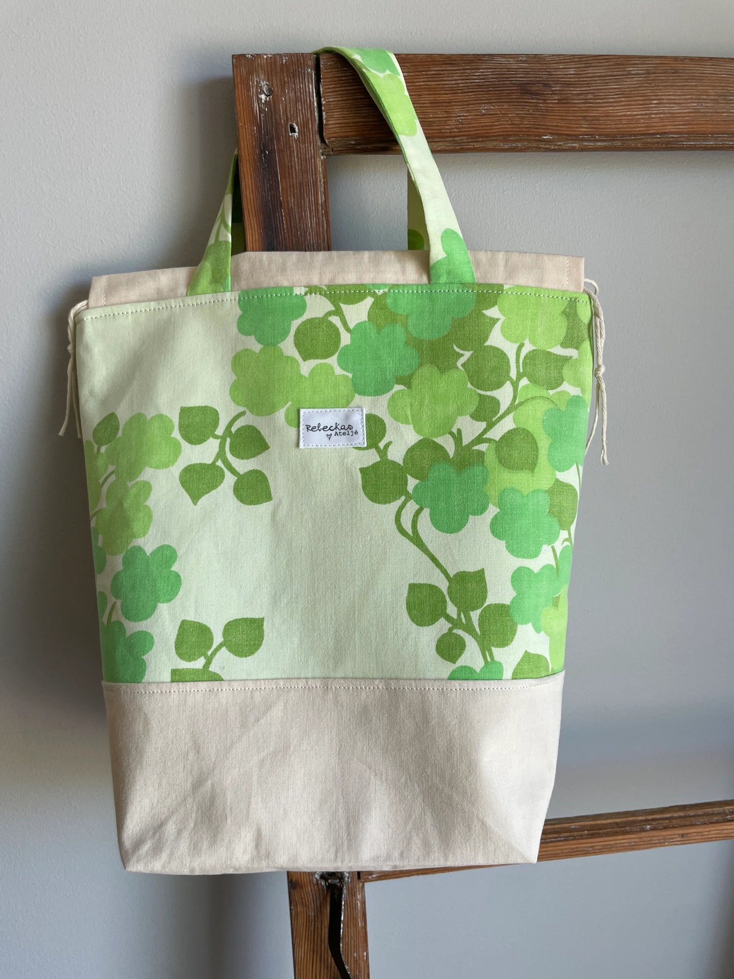 Projektväska mellan i ljusgult och grönt bomullstyg med retroinspirerat klövermönster i flera gröna nyanser. Handsydd projektpåse med dragskostängning och handtag, perfekt för stickning, virkning, garn och andra handarbetsprojekt. Den ljusgula bottenfärgen framhäver det gröna mönstret och ger väskan en ljus och somrig känsla.