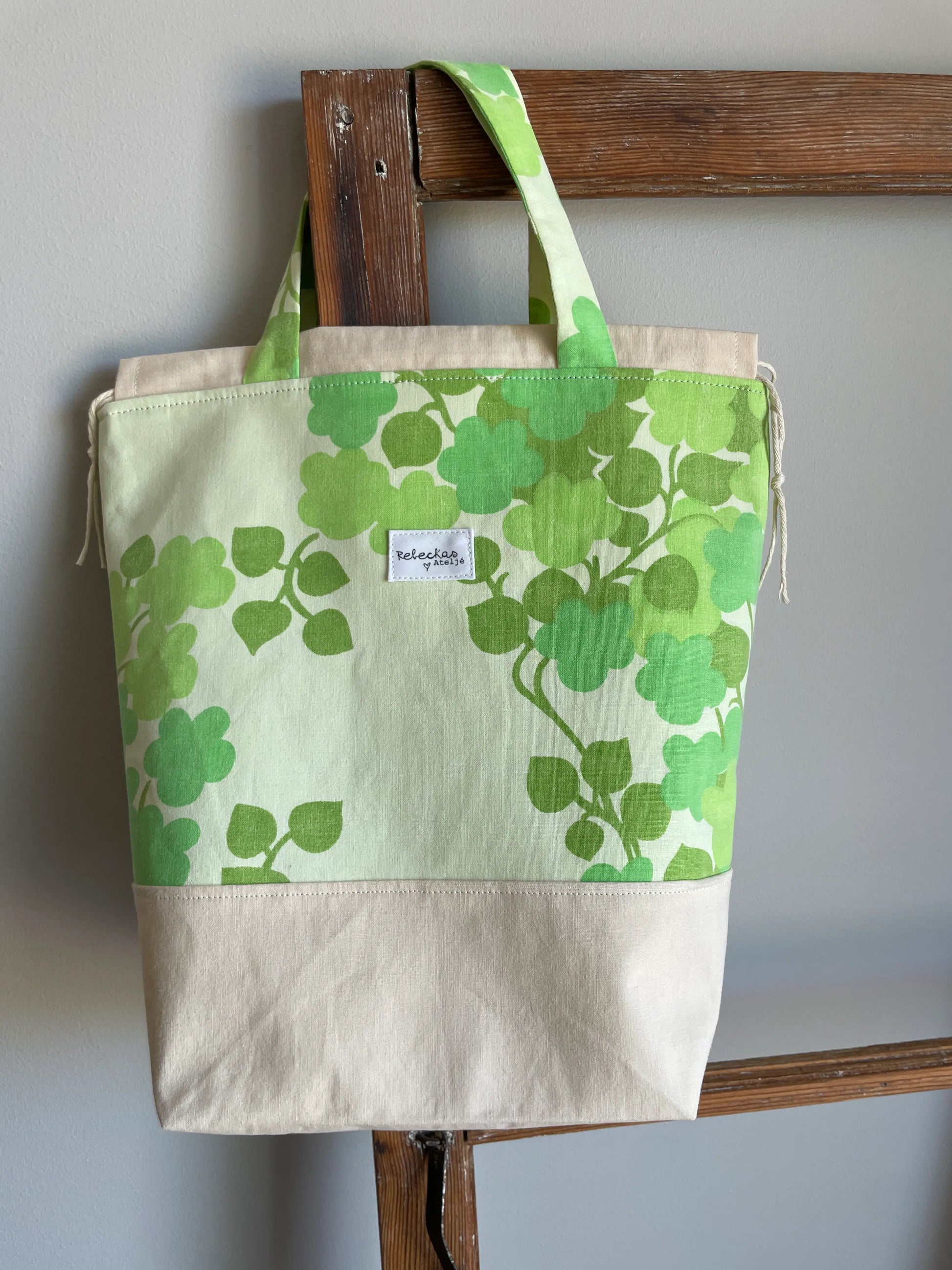 Projektväska mellan i ljusgult och grönt bomullstyg med retroinspirerat klövermönster i flera gröna nyanser. Handsydd projektpåse med dragskostängning och handtag, perfekt för stickning, virkning, garn och andra handarbetsprojekt. Den ljusgula bottenfärgen framhäver det gröna mönstret och ger väskan en ljus och somrig känsla.
