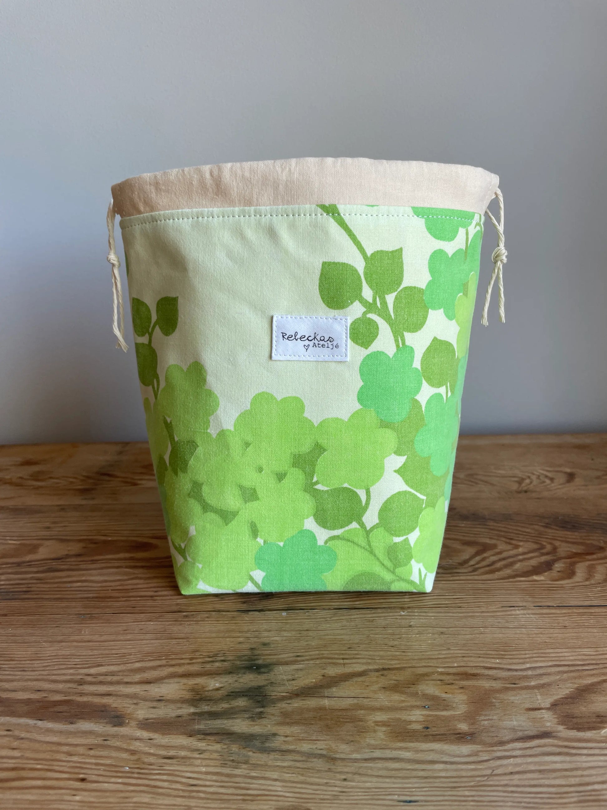 Handsydd liten projektpåse med dragsko i grönt bomullstyg med retroinspirerat blommönster. Praktisk förvaring för sockstickning, garn, virkning och andra mindre handarbetsprojekt. Rymlig projektväska i kompakt format för stickare och virkare.