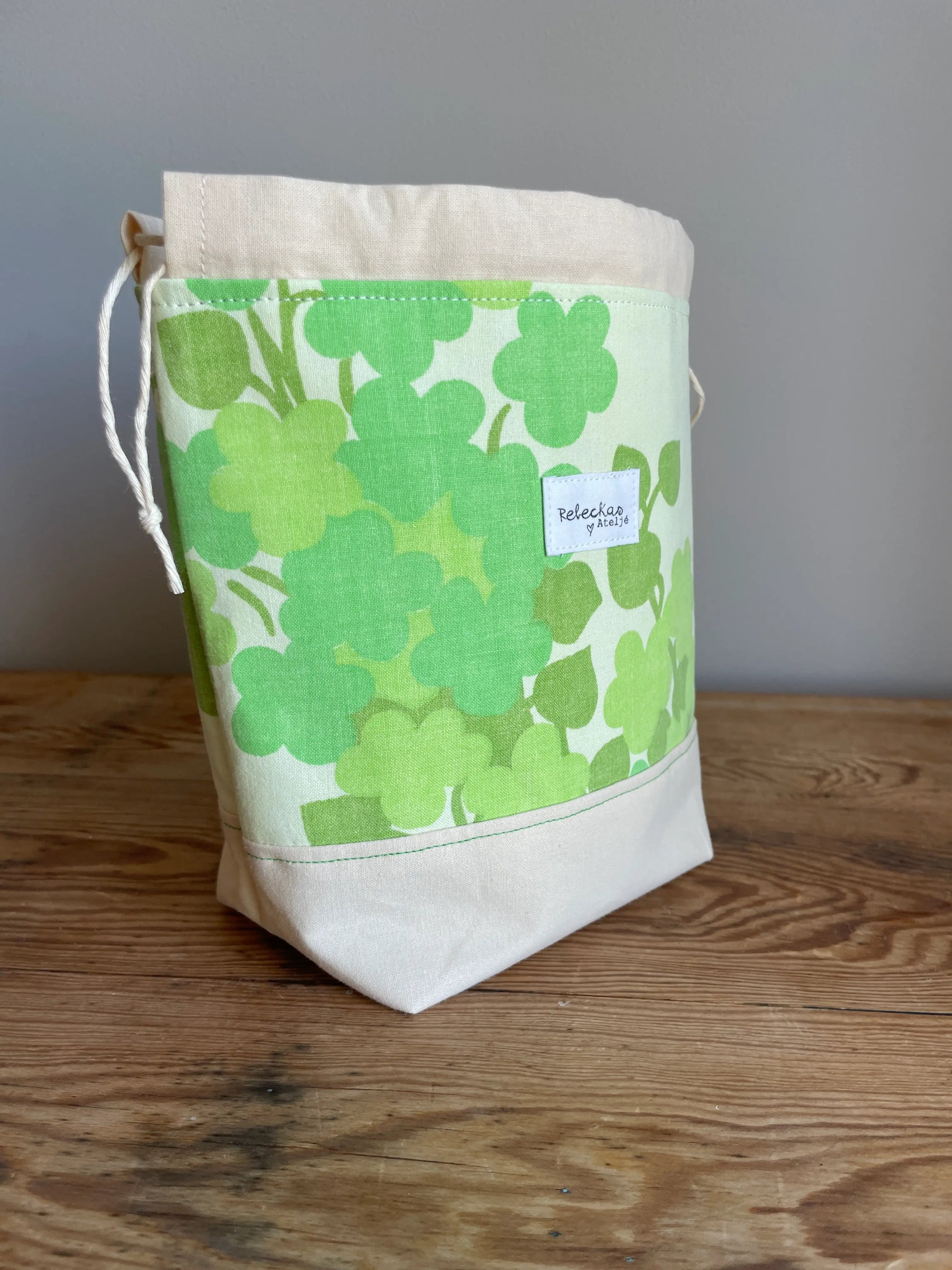 Liten projektpåse med dragsko i ljusgult bomullstyg med grönt retroinspirerat klövermönster. Handsydd projektpåse för mindre stick- och virkprojekt, garnförvaring samt tillbehör som maskmarkörer, stickor och virknålar. Den ljusgula bottenfärgen och de gröna nyanserna ger väskan en ljus, somrig och nostalgisk känsla.
