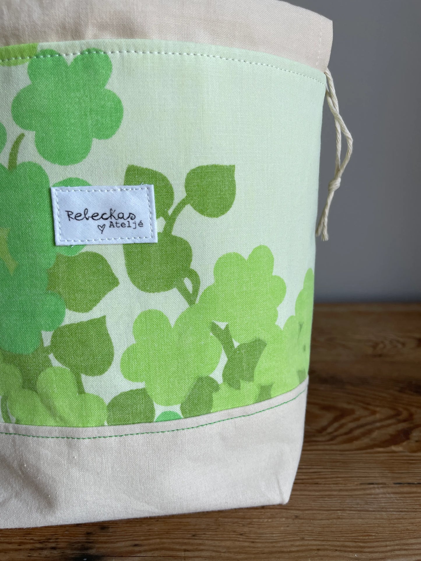 Liten projektpåse med dragsko i ljusgult bomullstyg med grönt retroinspirerat klövermönster. Handsydd projektpåse för mindre stick- och virkprojekt, garnförvaring samt tillbehör som maskmarkörer, stickor och virknålar. Den ljusgula bottenfärgen och de gröna nyanserna ger väskan en ljus, somrig och nostalgisk känsla.
