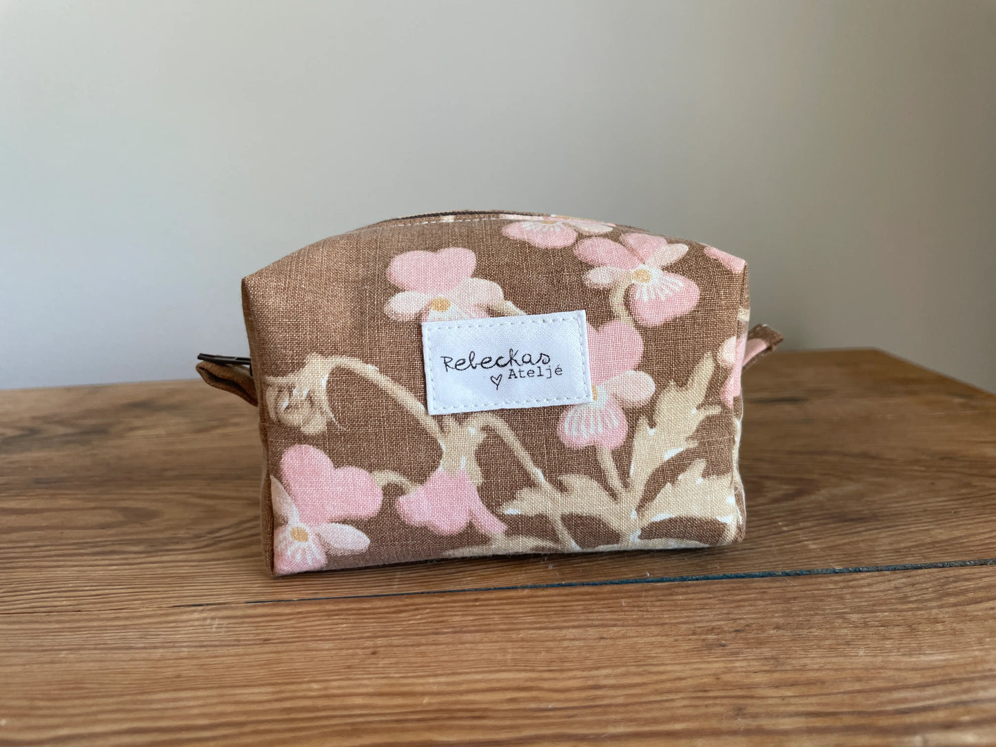 Mini boxnecessär i brun bomull med romantiskt blommönster i rosa, beige, creme och honungsgula toner. Handsydd necessär med rymlig boxform för smink, toalettartiklar, sticktillbehör och annan praktisk förvaring. Det vintageinspirerade blommönstret ger en varm, nostalgisk känsla med lantlig charm.