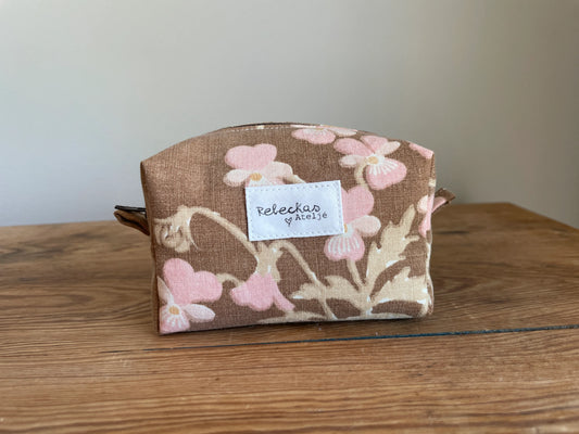 Mini boxnecessär i brun bomull med romantiskt blommönster i rosa, beige, creme och honungsgula toner. Handsydd necessär med rymlig boxform för smink, toalettartiklar, sticktillbehör och annan praktisk förvaring. Det vintageinspirerade blommönstret ger en varm, nostalgisk känsla med lantlig charm.