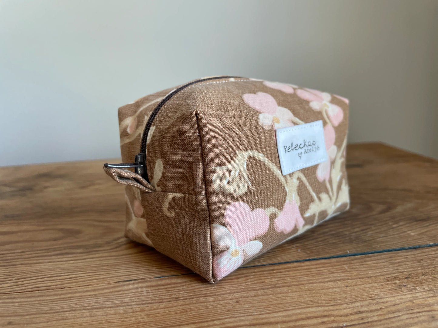 Mini boxnecessär i brun bomull med romantiskt blommönster i rosa, beige, creme och honungsgula toner. Handsydd necessär med rymlig boxform för smink, toalettartiklar, sticktillbehör och annan praktisk förvaring. Det vintageinspirerade blommönstret ger en varm, nostalgisk känsla med lantlig charm.